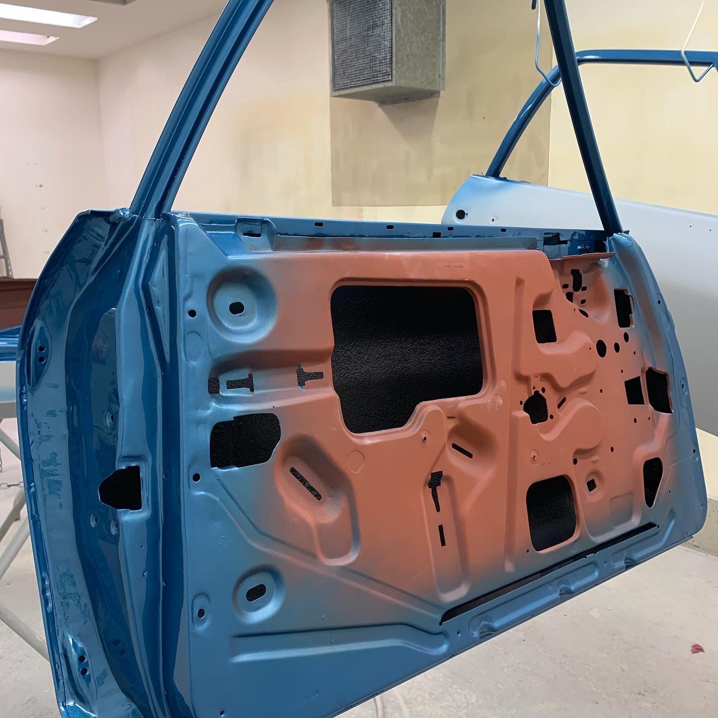 Blue car door panel with exposed orange inner metal and wiring, shown in a workshop setting