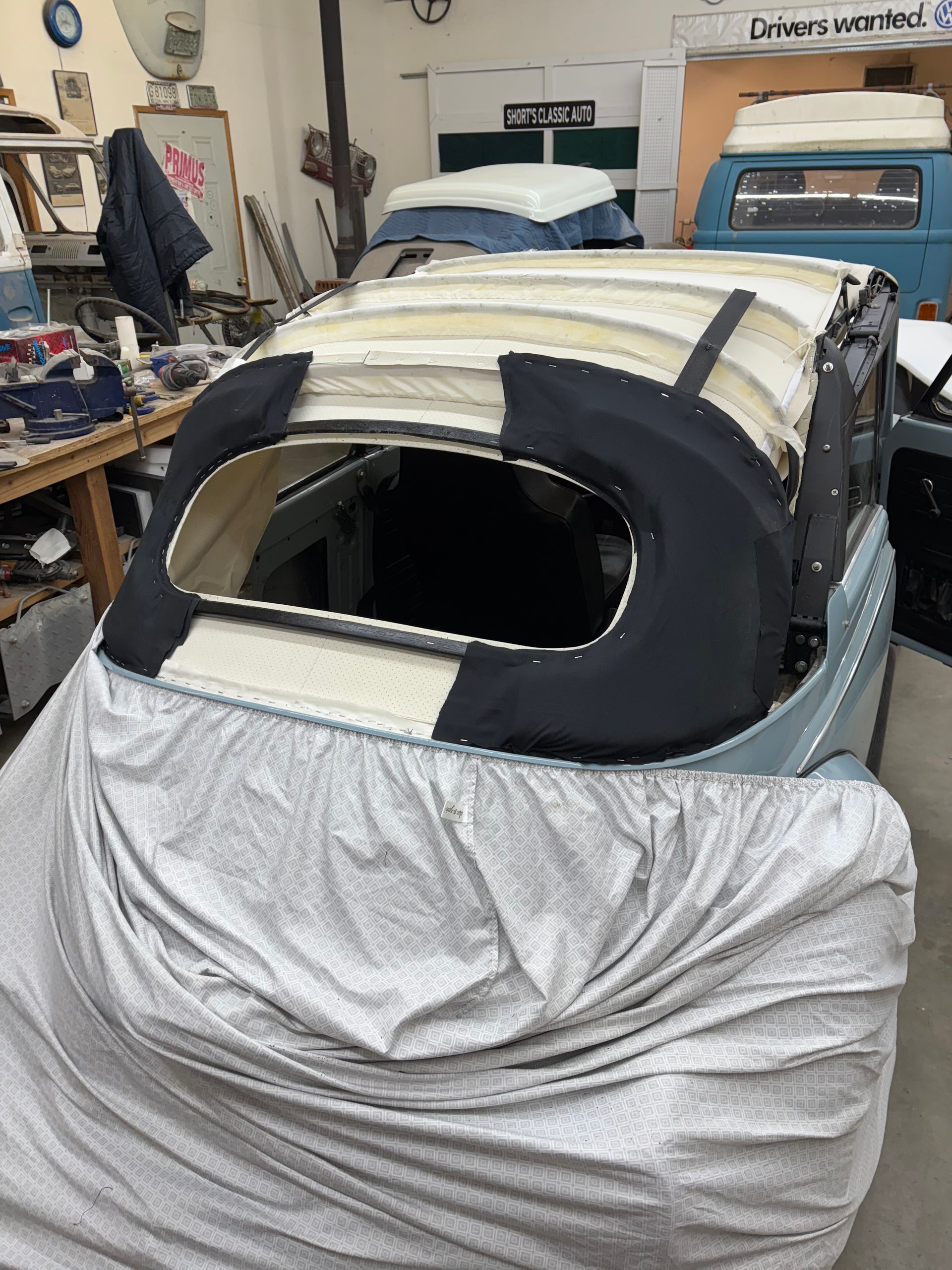Convertible car roof under repair in a garage, covered with tape and a cloth drape.