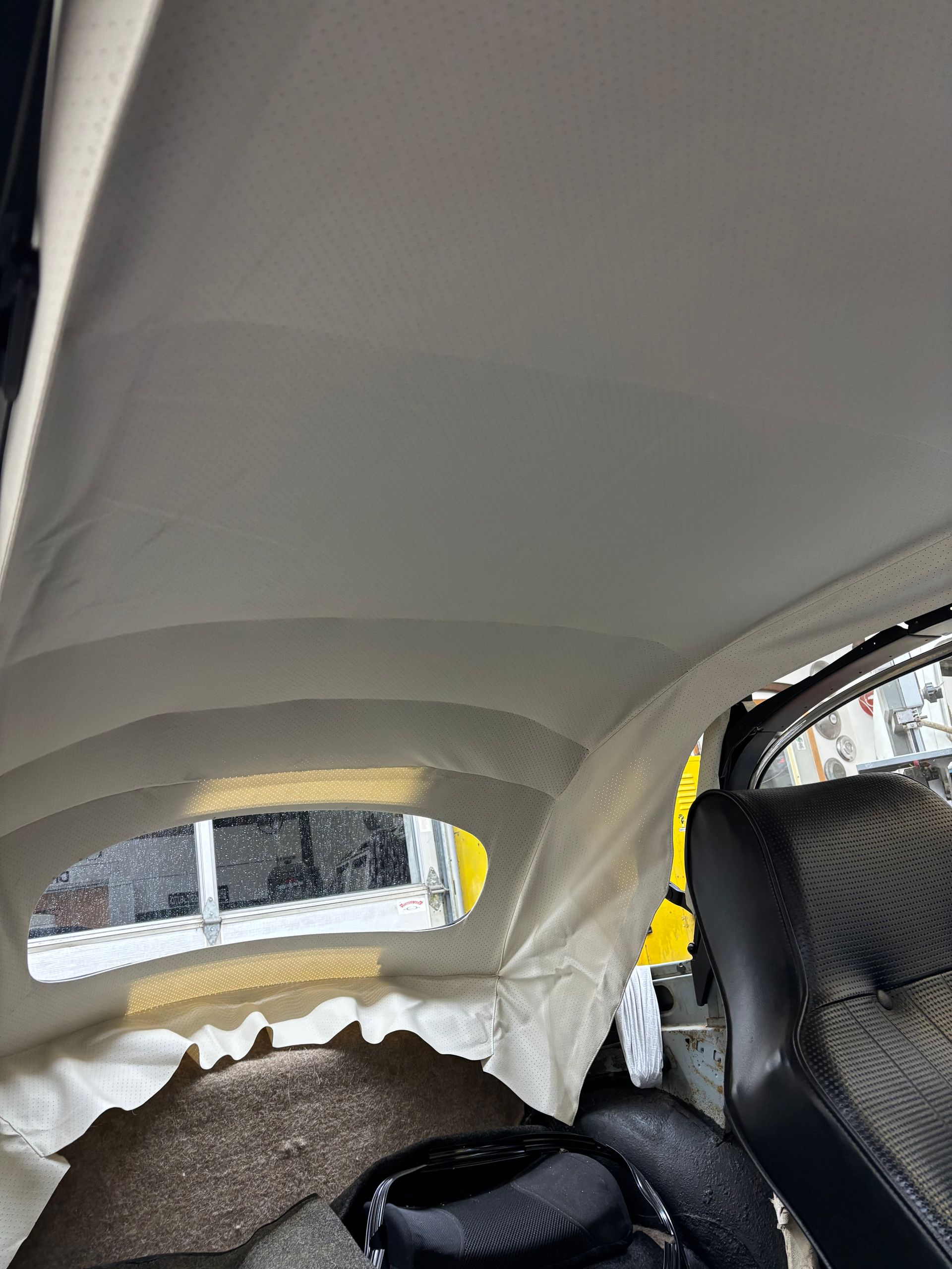 Car interior with a white headliner, rear window, and a black child car seat on the right.