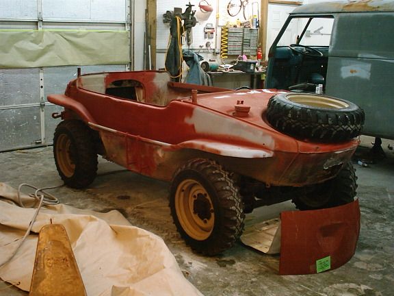 Red off-road custom car body in a workshop, with a spare tire mounted on the rear.