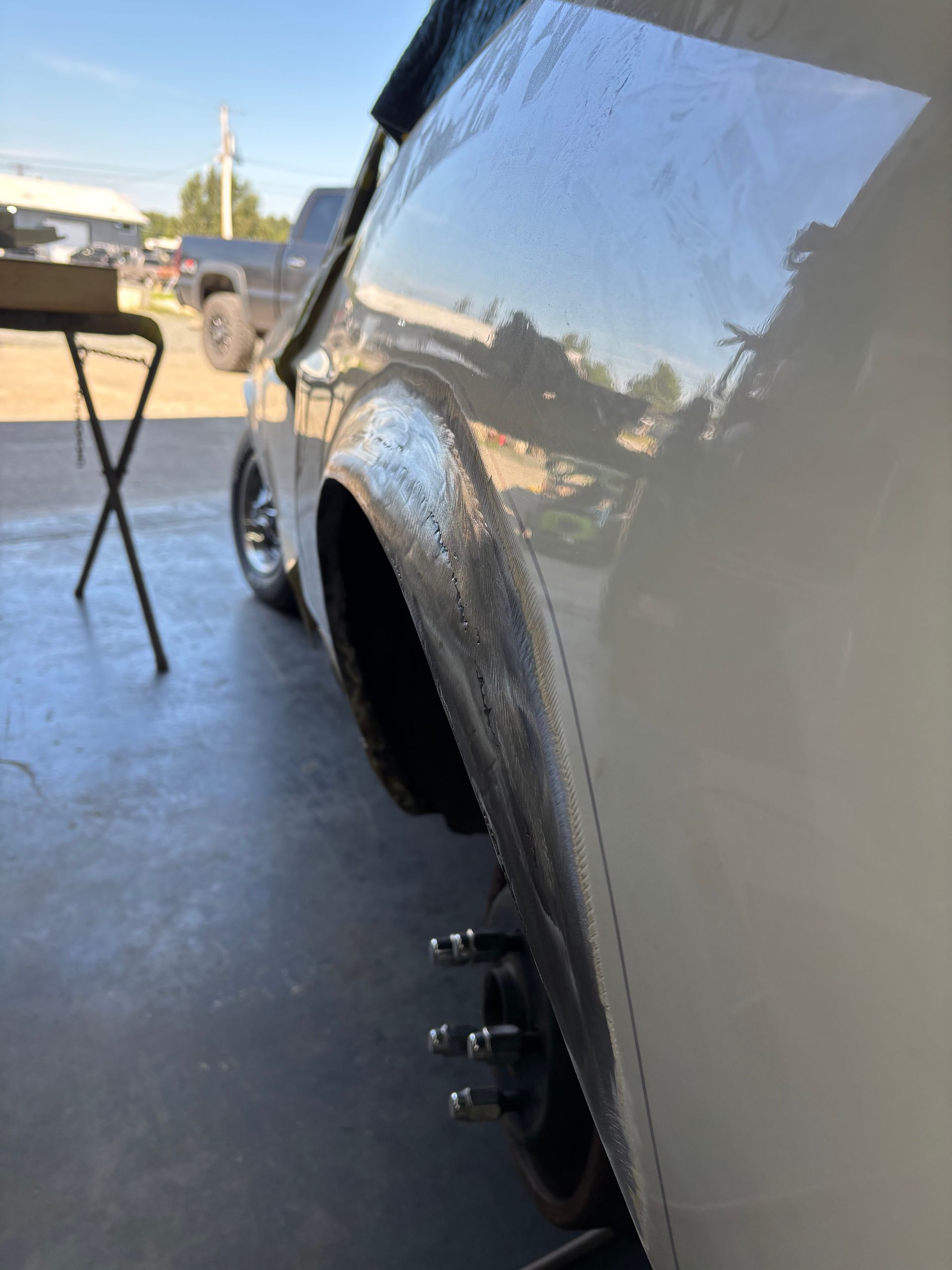 White car with rear wheel removed, showing exposed wheel studs in a driveway or garage.