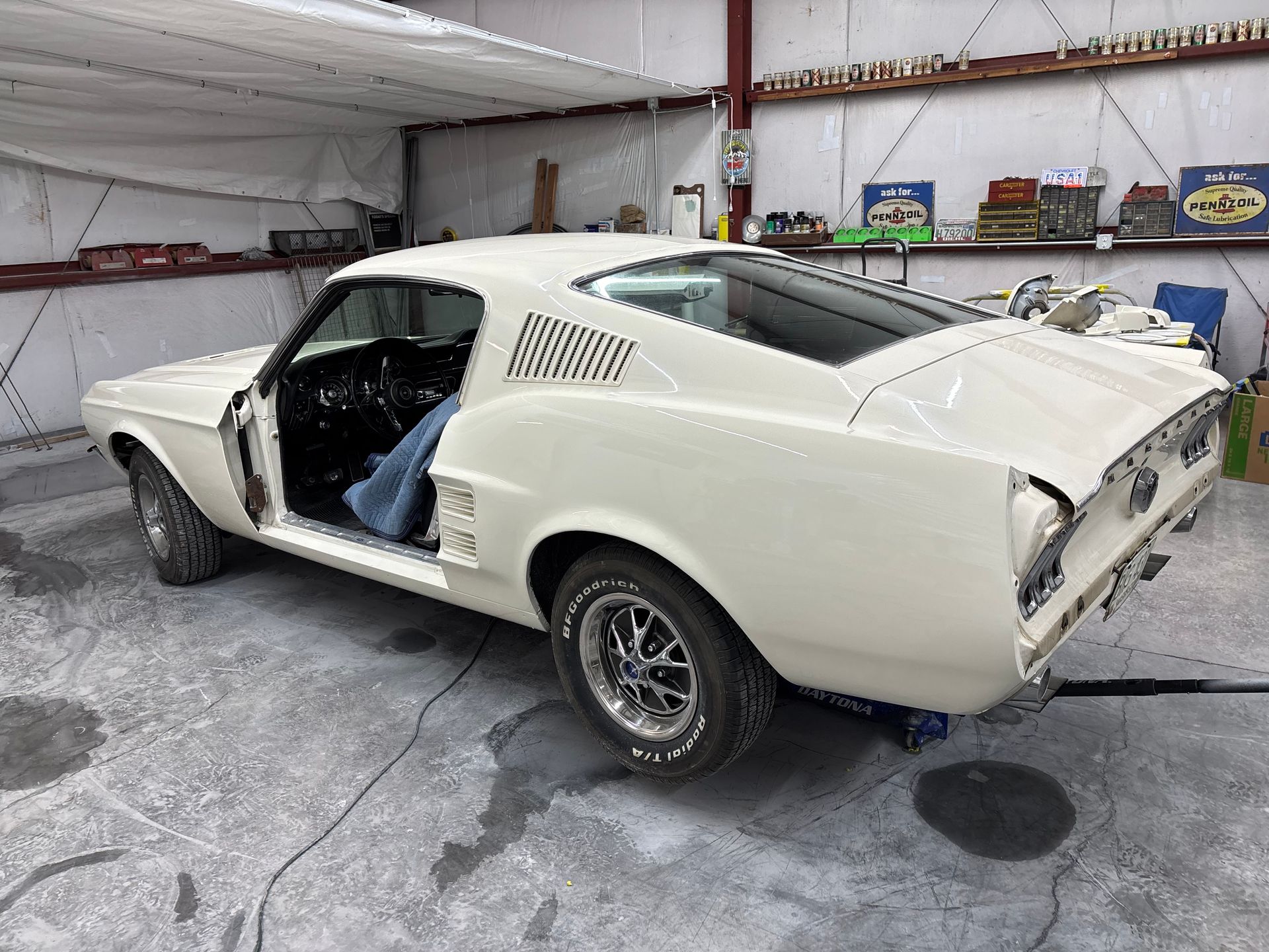 White classic sports car in a garage, viewed from the rear with the driver’s door open.