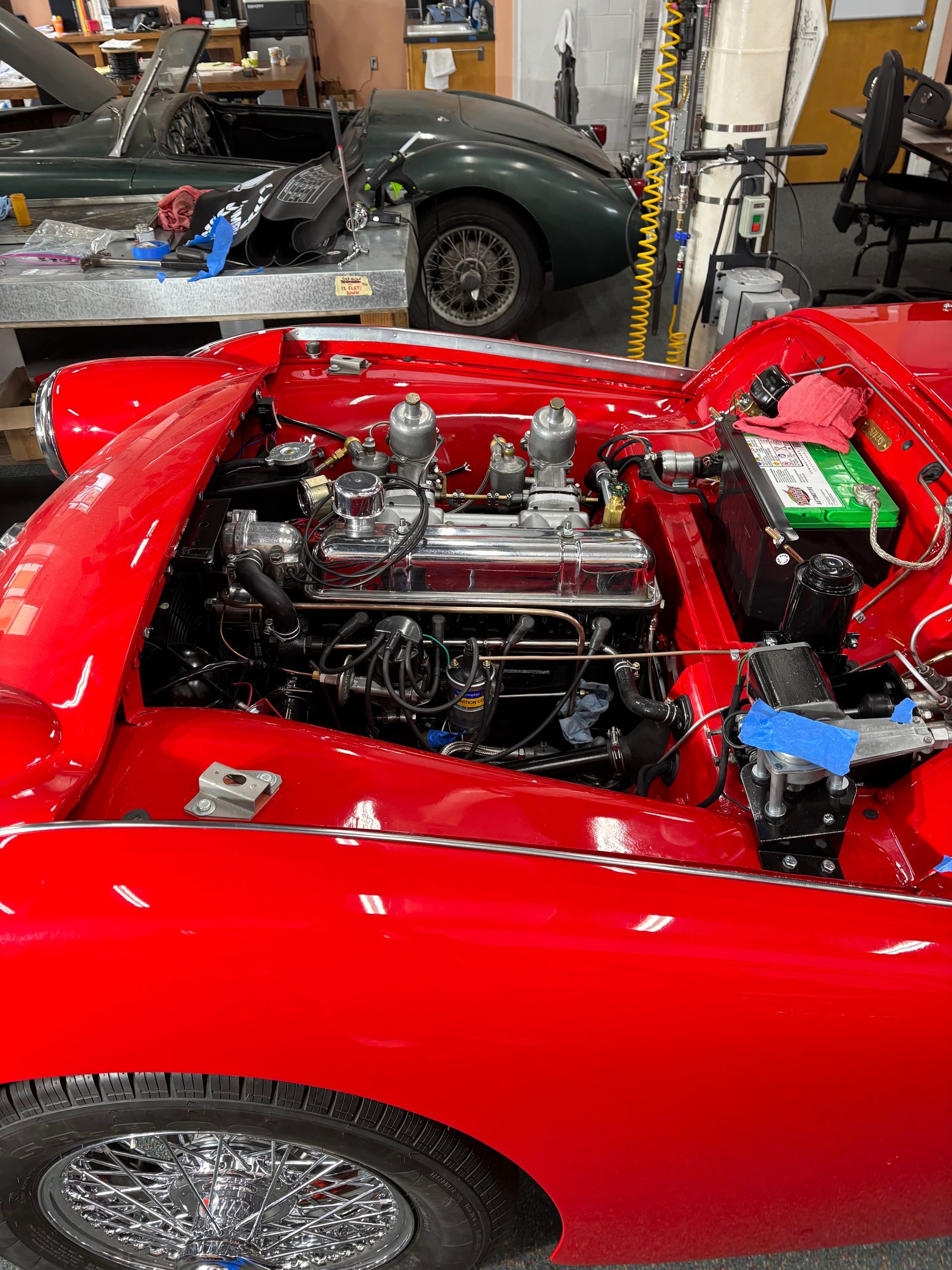 Red classic car with open engine bay in a garage, showing chrome engine parts and bright red body.