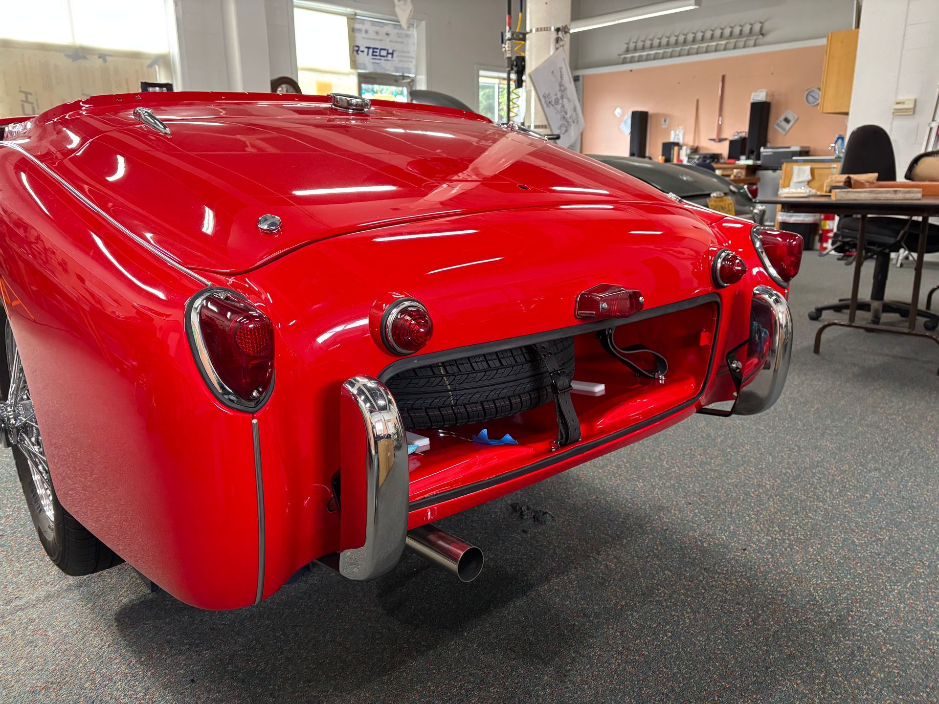 Red vintage sports car in a garage, rear view with chrome bumper and rounded taillights.