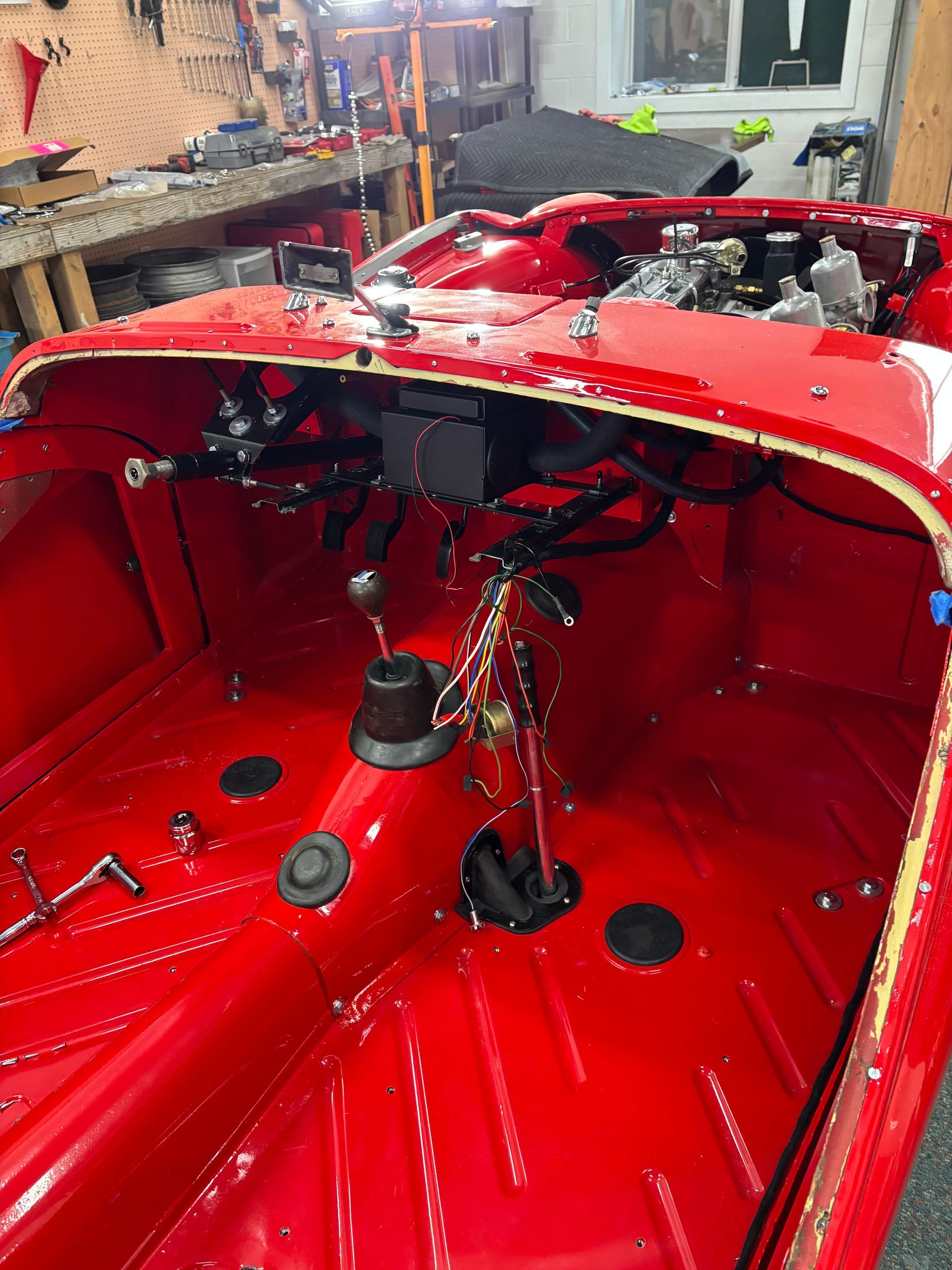 Red boat interior in a workshop, with exposed wiring, controls, and a central gear lever.