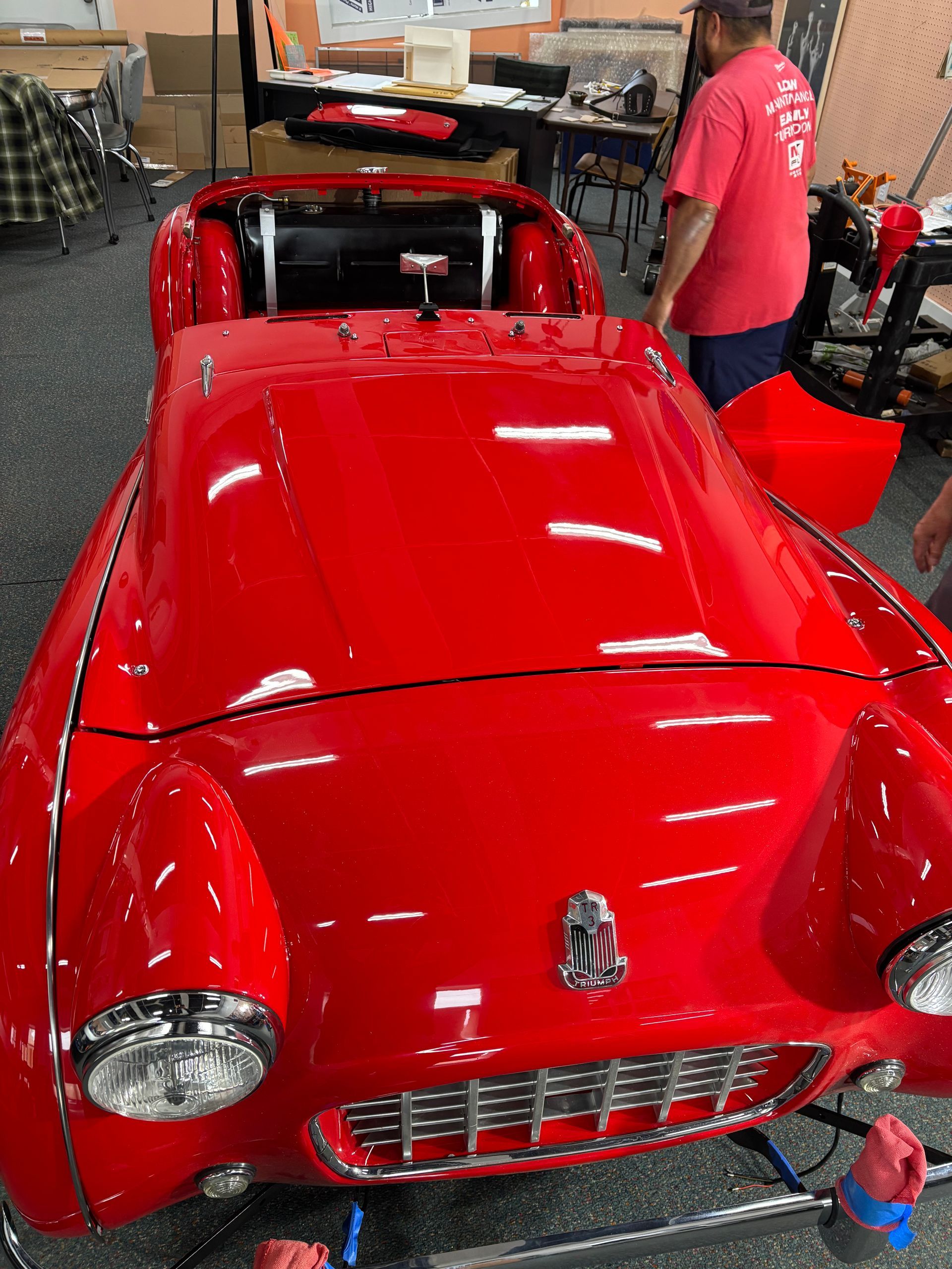 Shiny red classic car displayed indoors with a person standing beside it