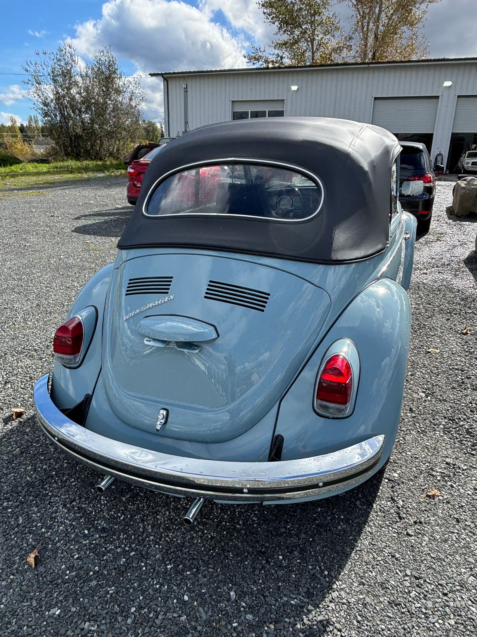 Light blue vintage convertible with black top parked on gravel near a building