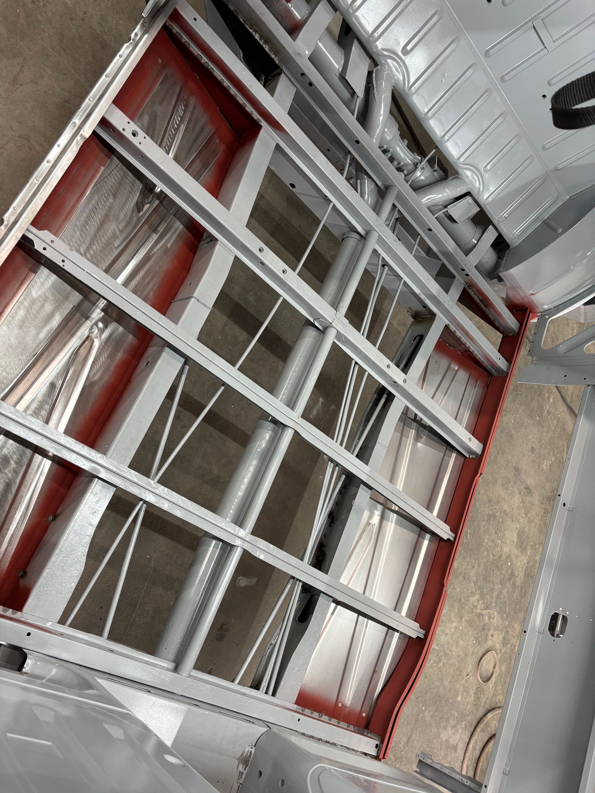 Aluminum ladder-like frame with red supports, lying inside a truck or trailer cargo area.
