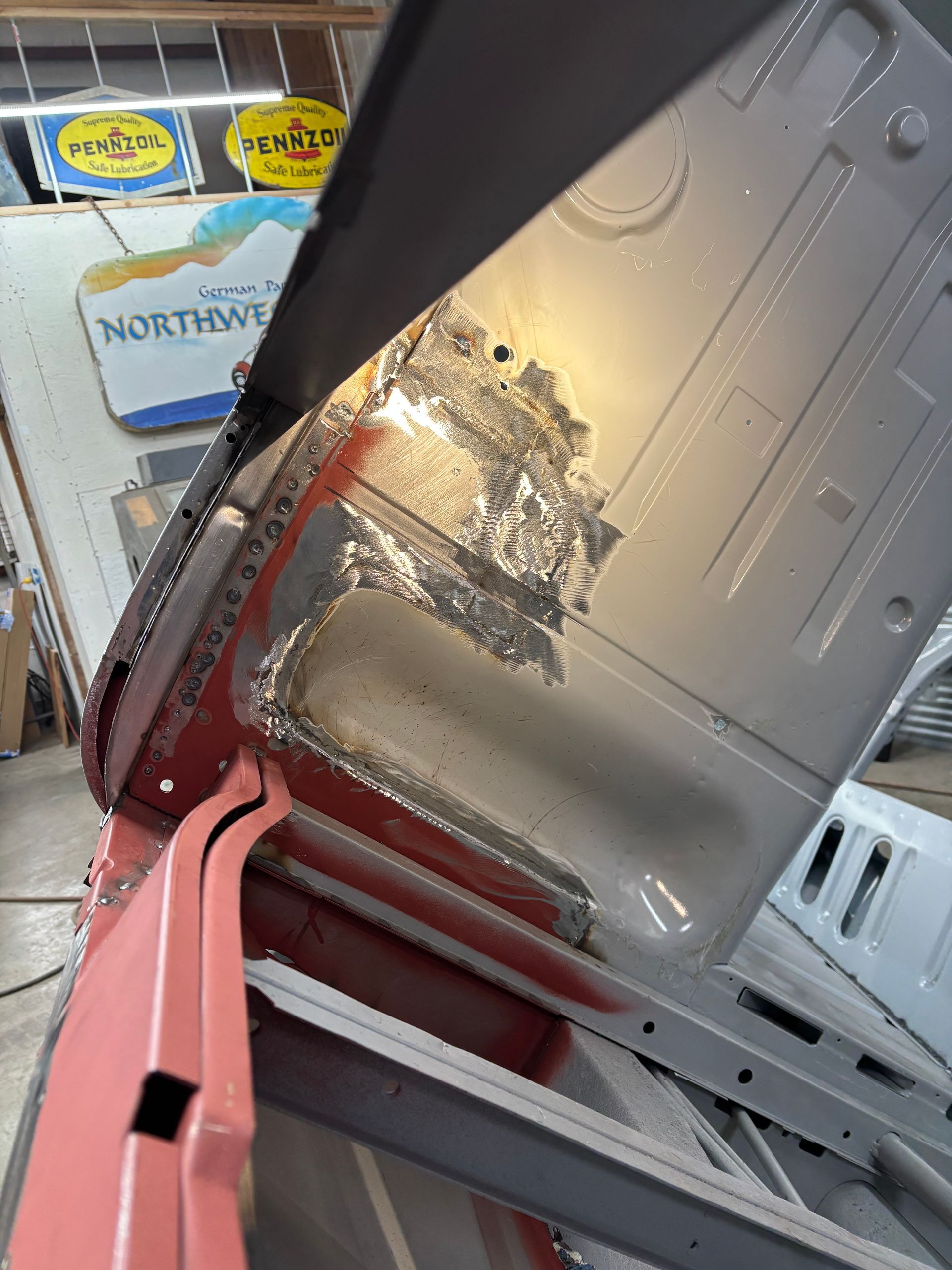Close-up of a damaged gray car body panel with a scraped, rusted area in a garage or workshop.