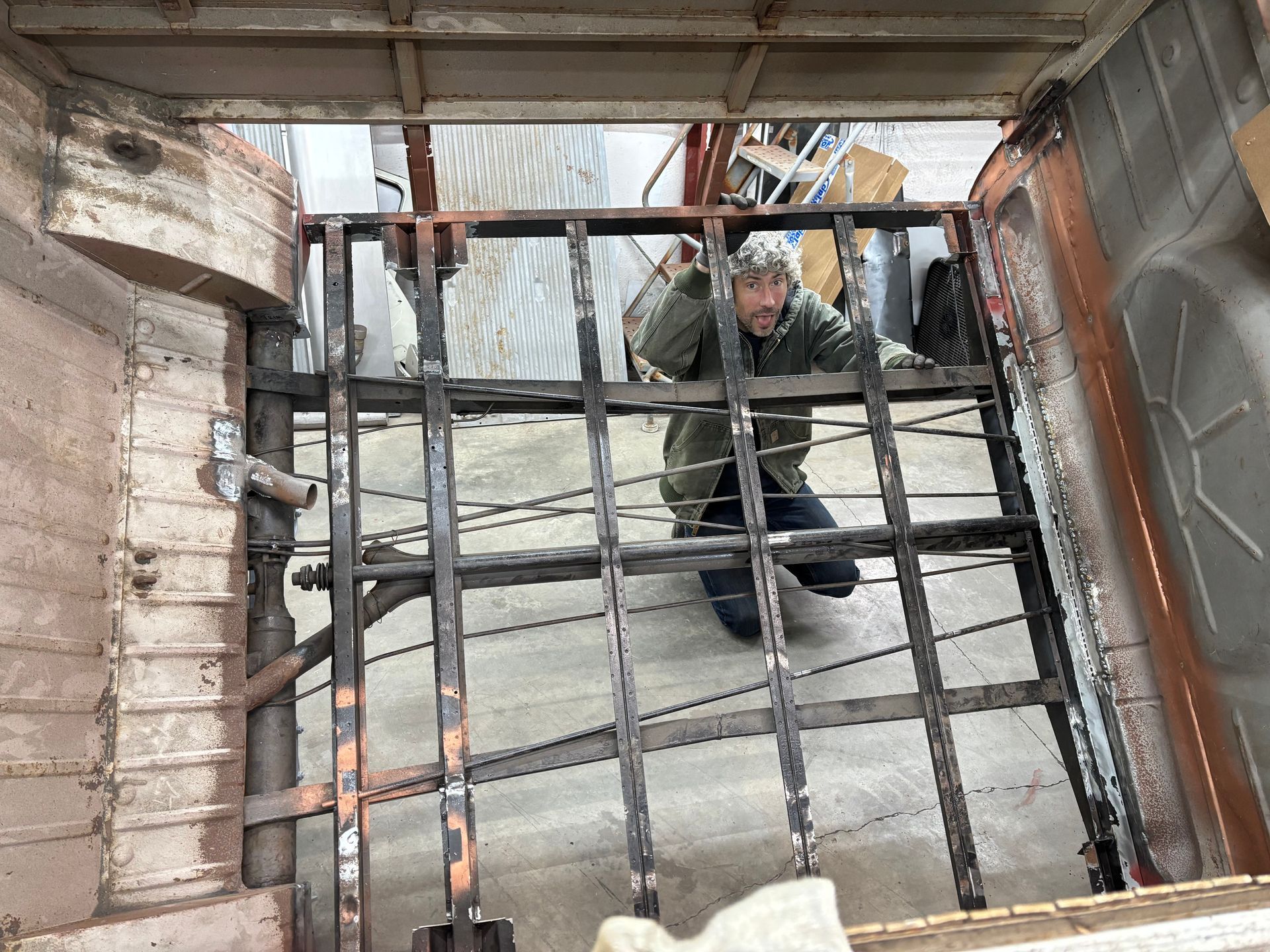 Person crouching behind a black metal gate in a weathered industrial corridor.