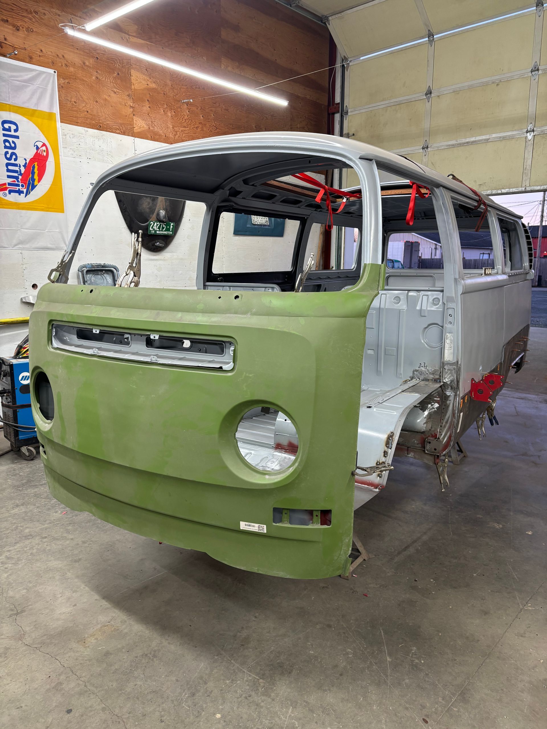 Partially painted green and gray van body in a workshop with exposed interior.