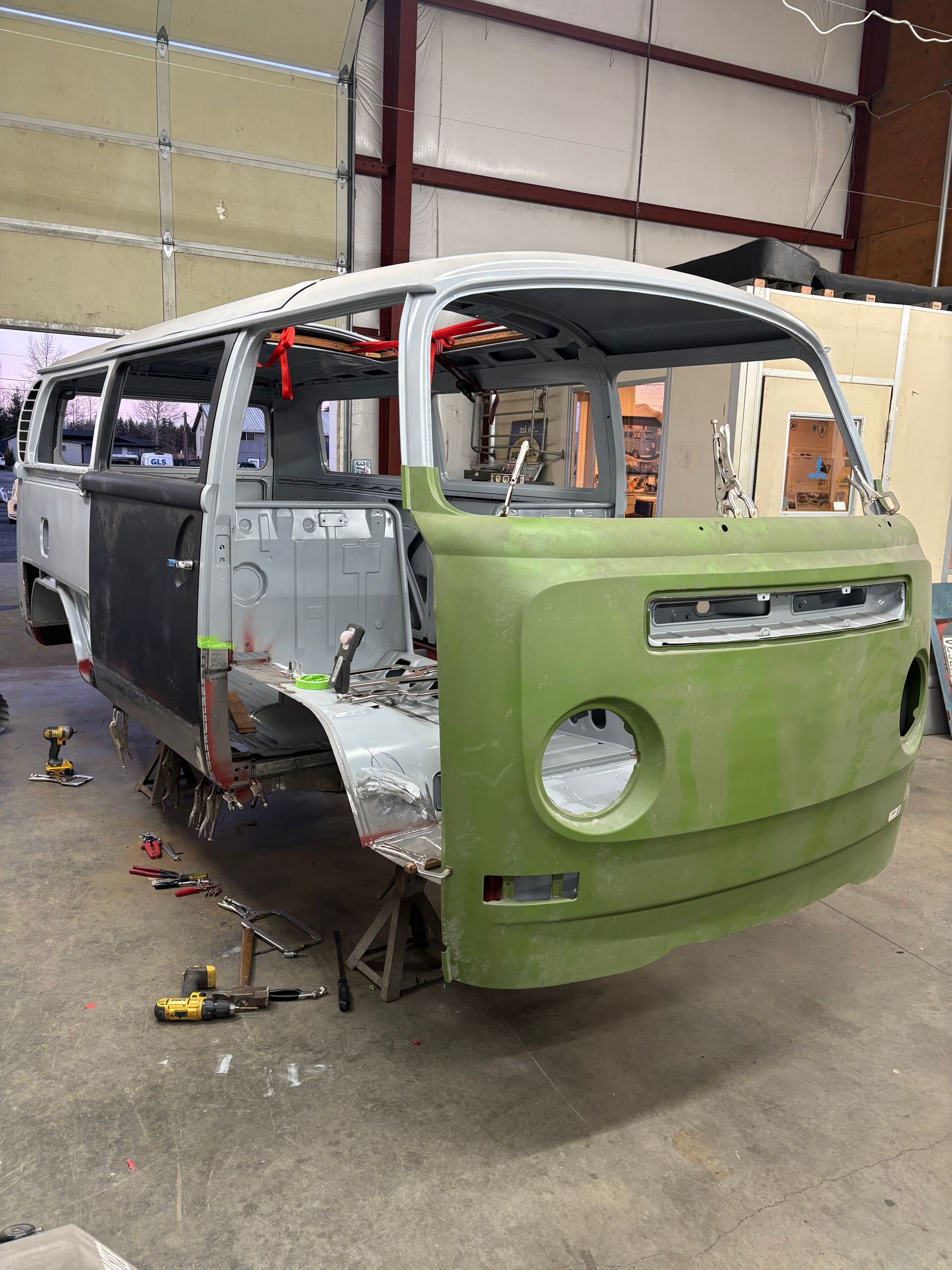 Partially assembled green-and-gray van body inside a workshop, missing panels and front lights.