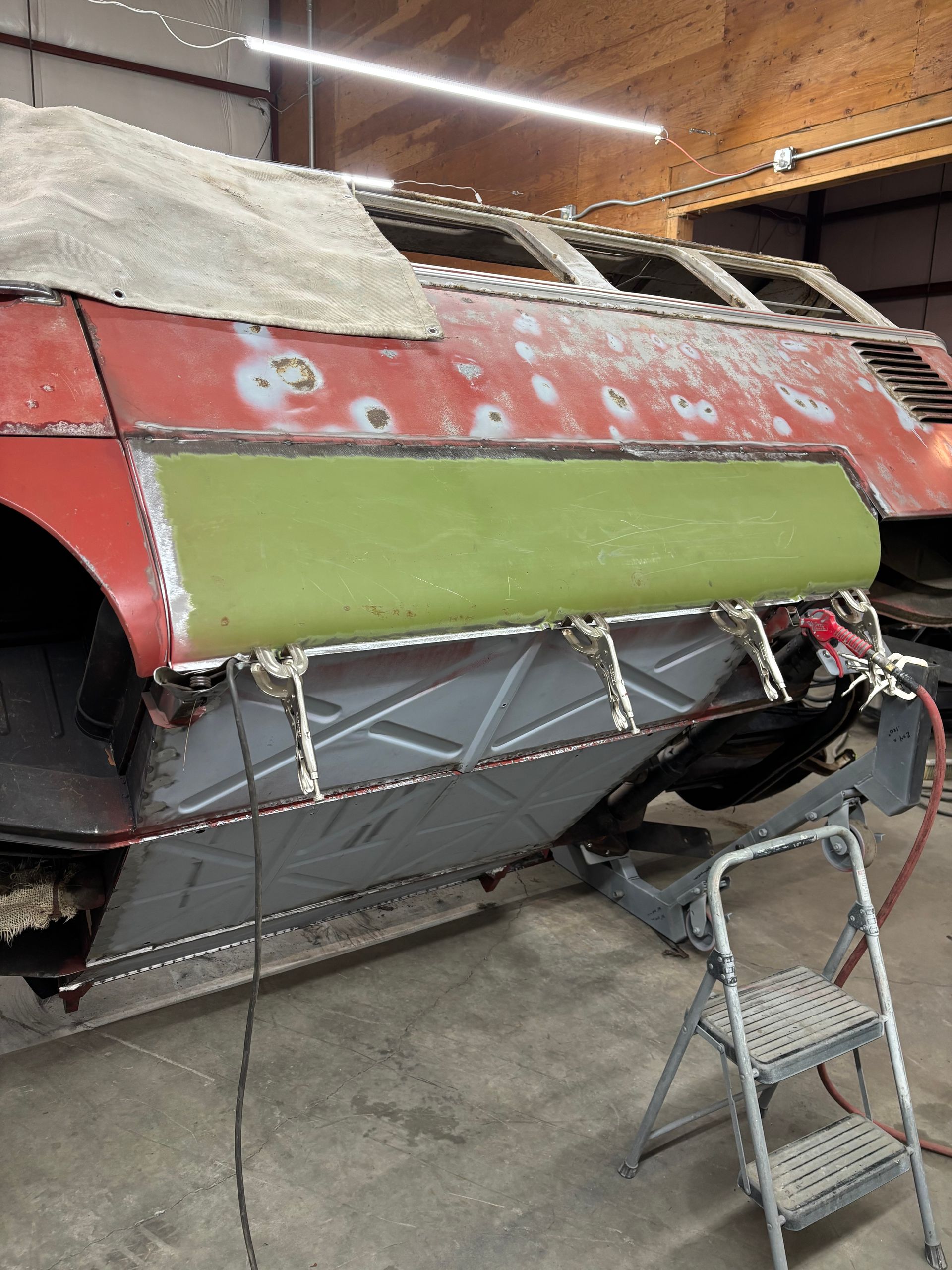 Partially restored red vehicle body in a workshop, with green primer and a step ladder nearby