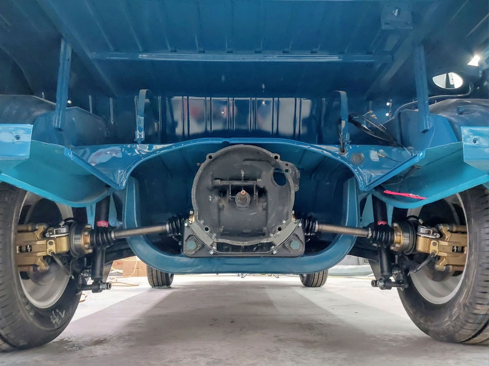 Low-angle view of a blue car’s undercarriage and rear suspension on a lift, with wheels visible on both sides