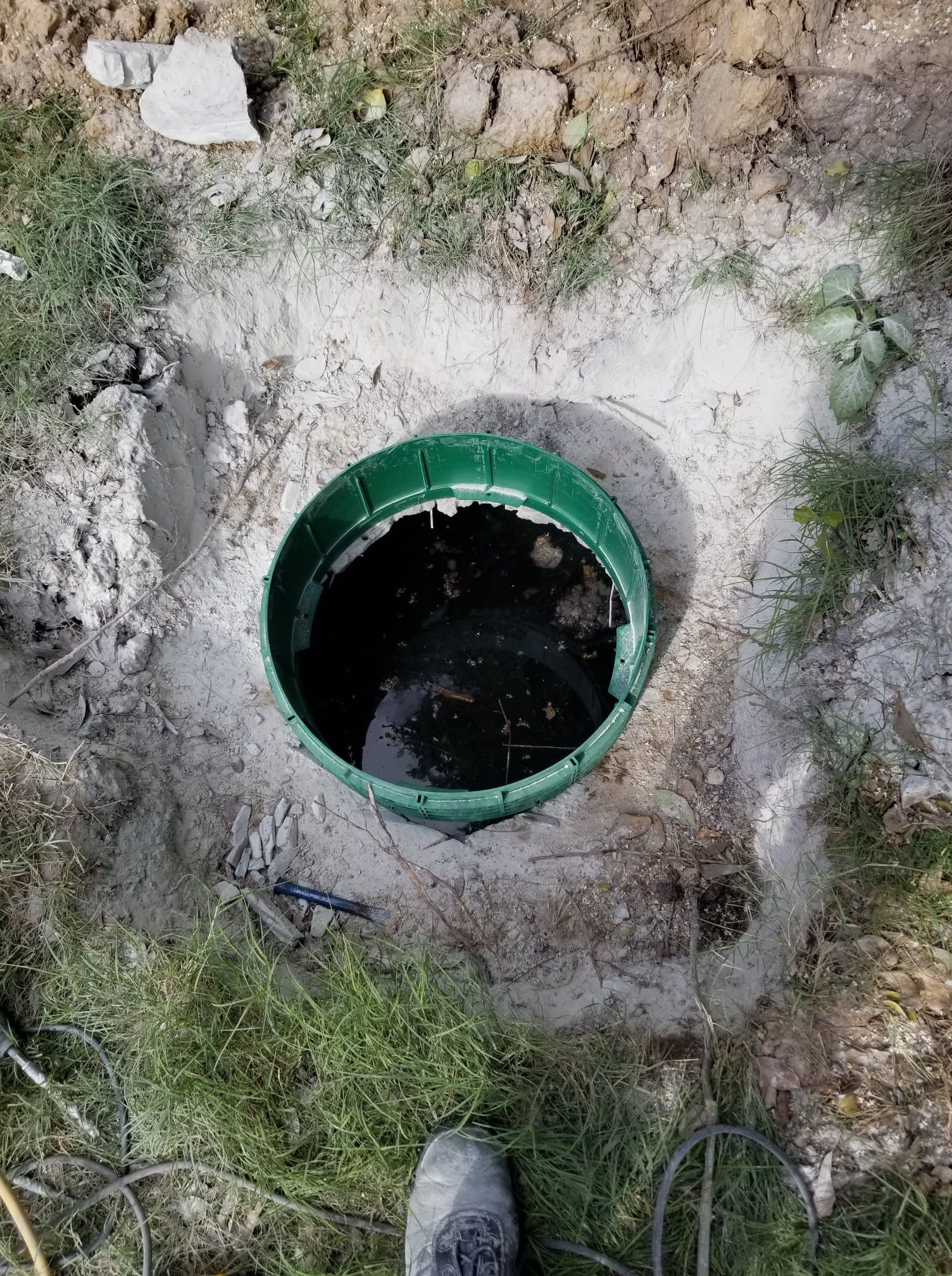Green septic tank lid open, surrounded by dirt and grass. Black liquid visible inside.