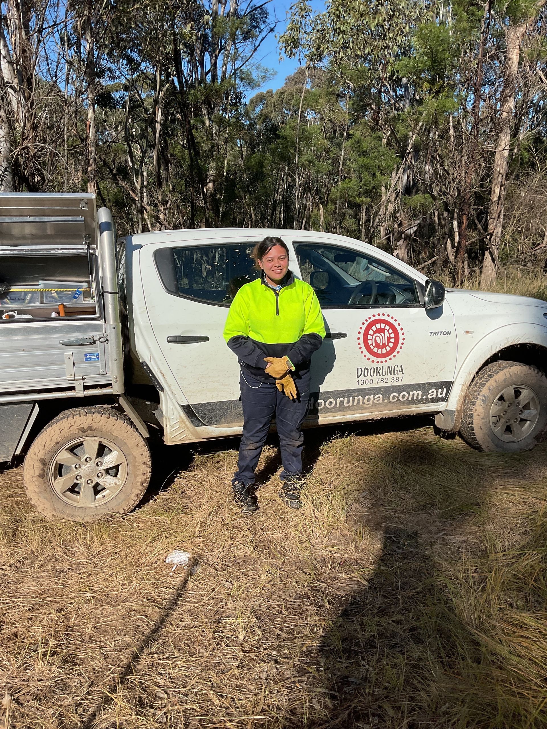 A woman is standing in front of a truck in a field.