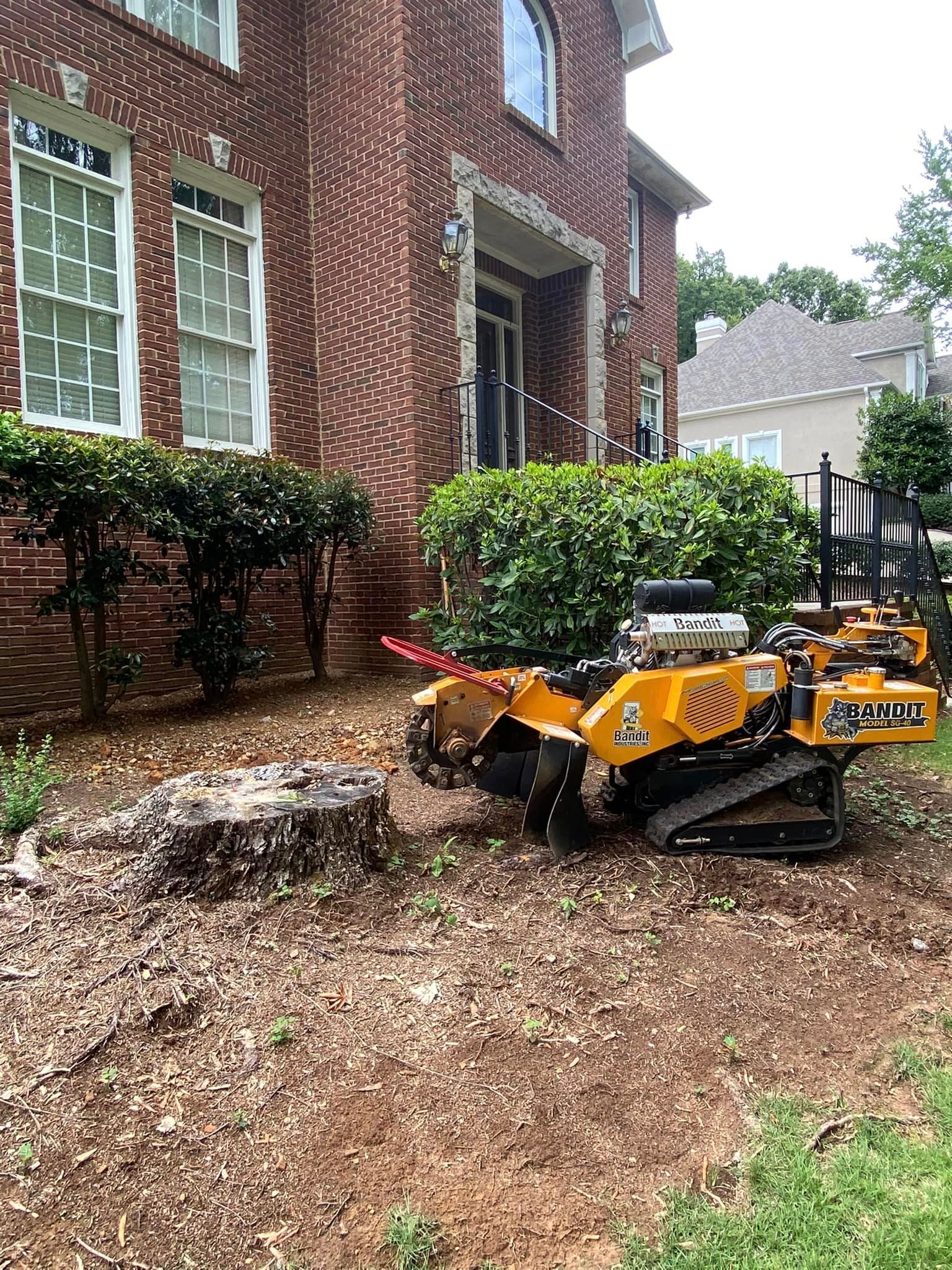 A stump grinder is sitting in front of a brick house.