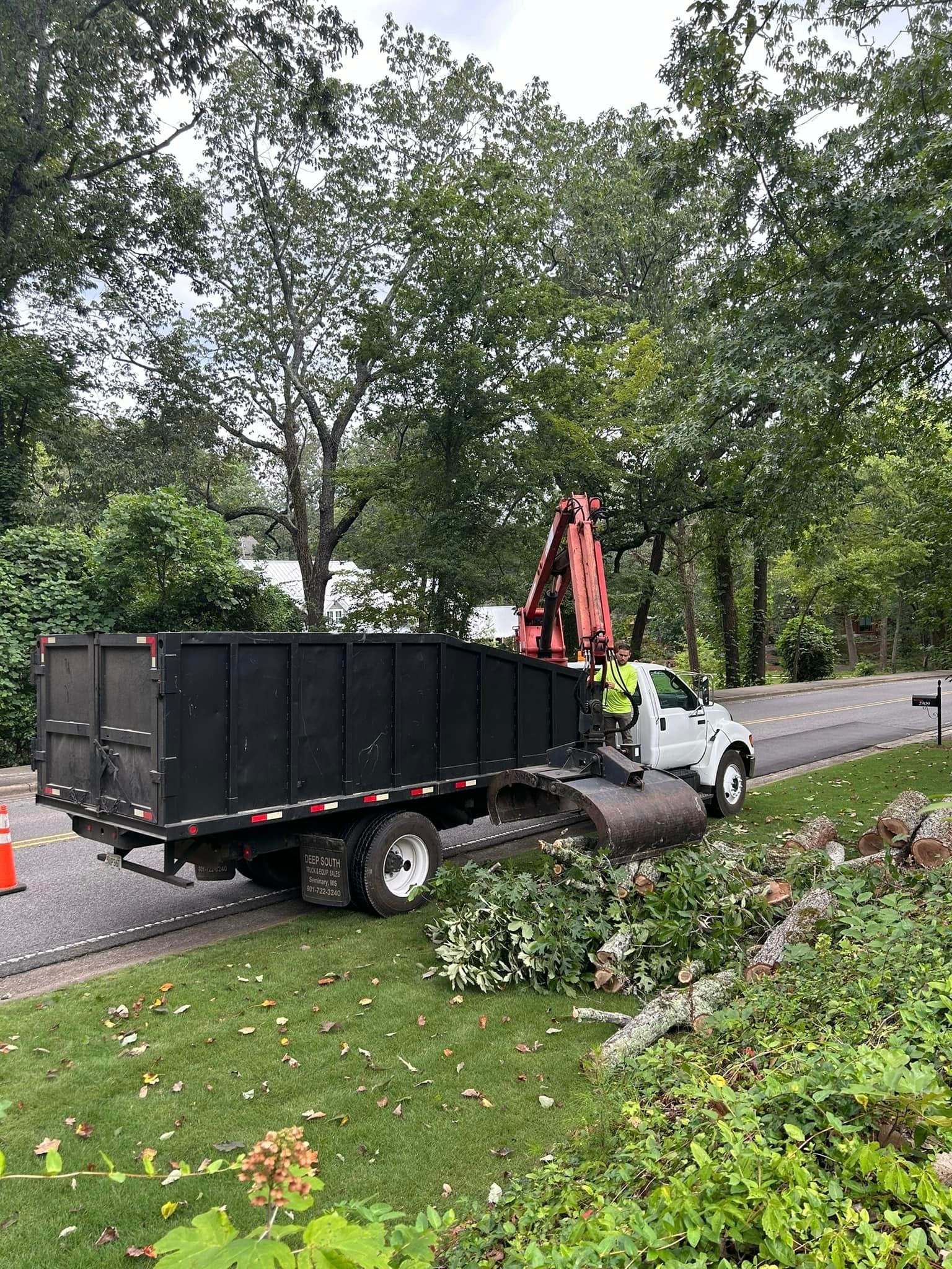 A dump truck with a crane attached to it is parked on the side of the road.