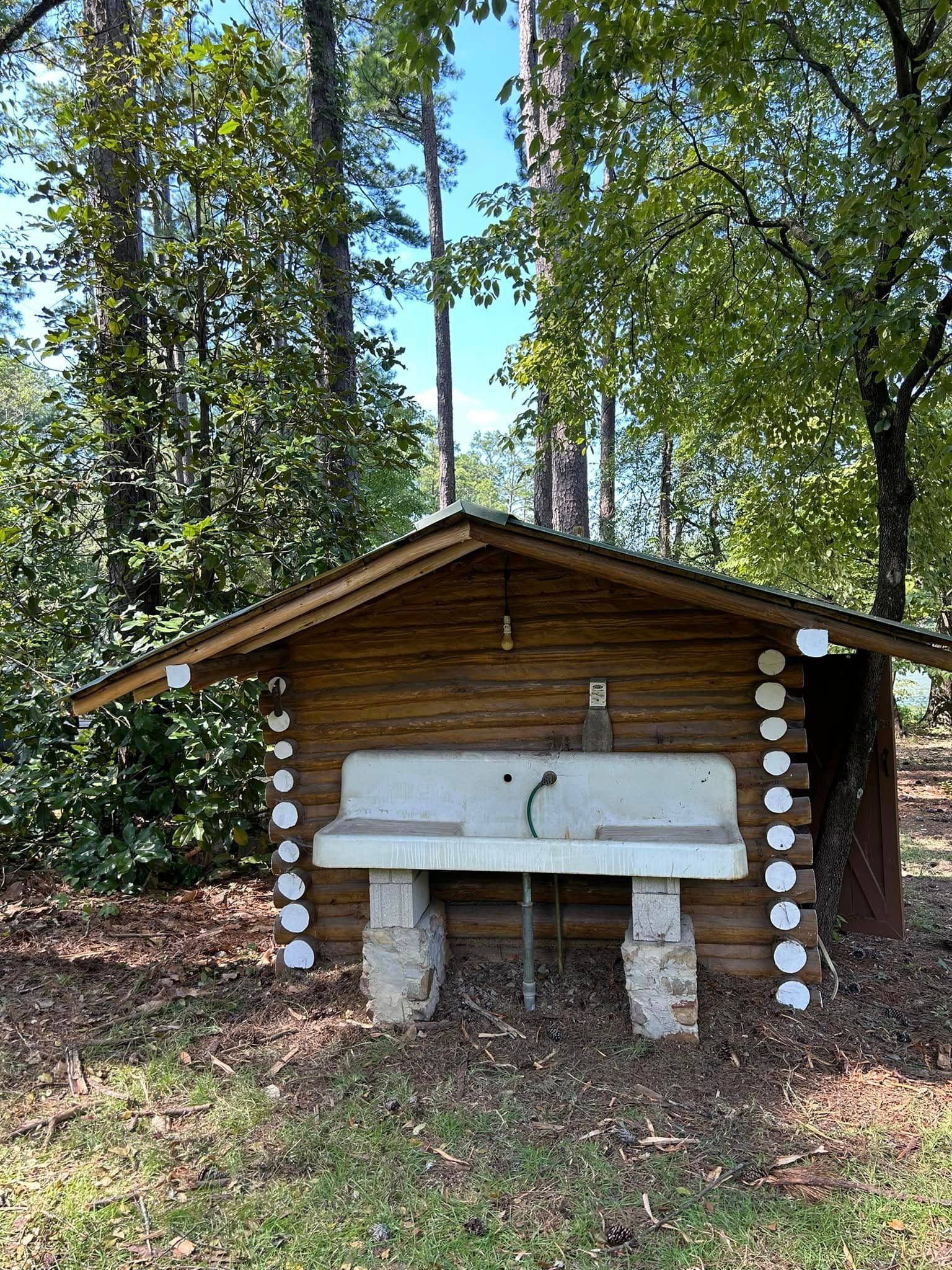 A wooden shack with a sink in the middle of the woods.