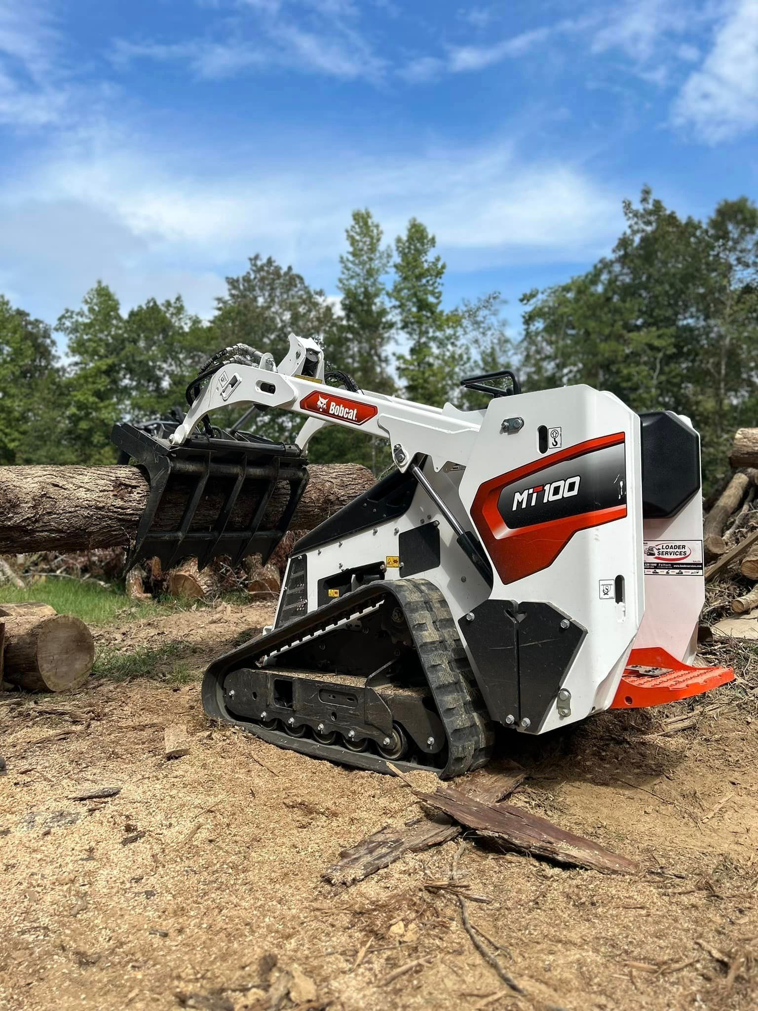 A bulldozer is sitting in the dirt next to a pile of logs.
