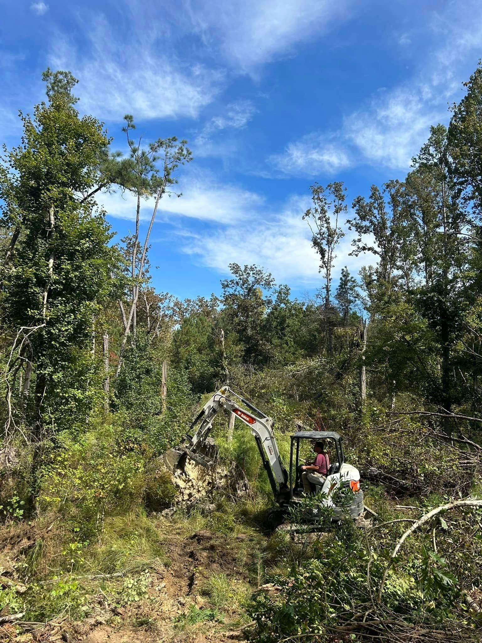 A man is driving an excavator through a forest.