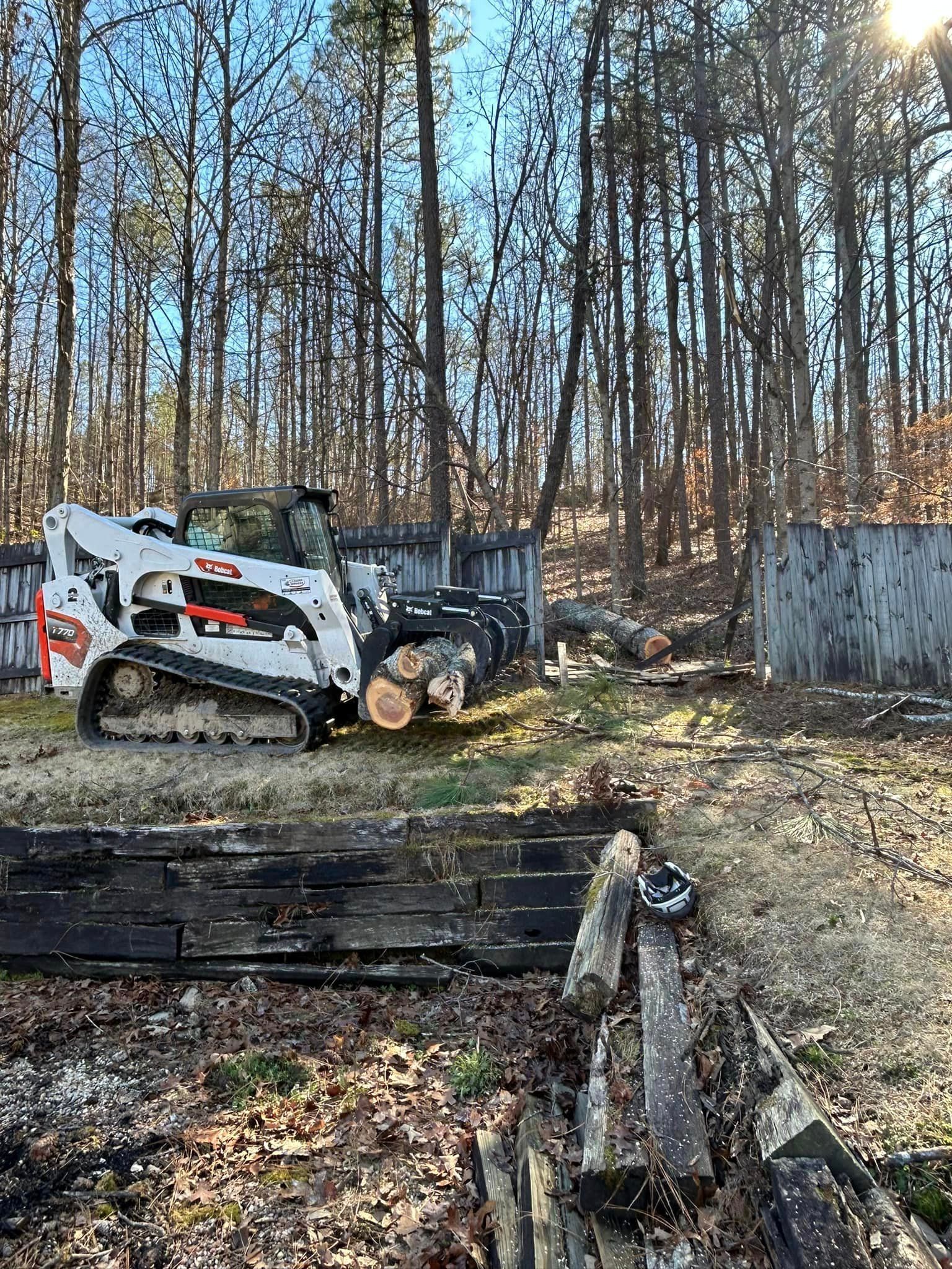 A bulldozer is sitting in the middle of a forest next to a pile of logs.