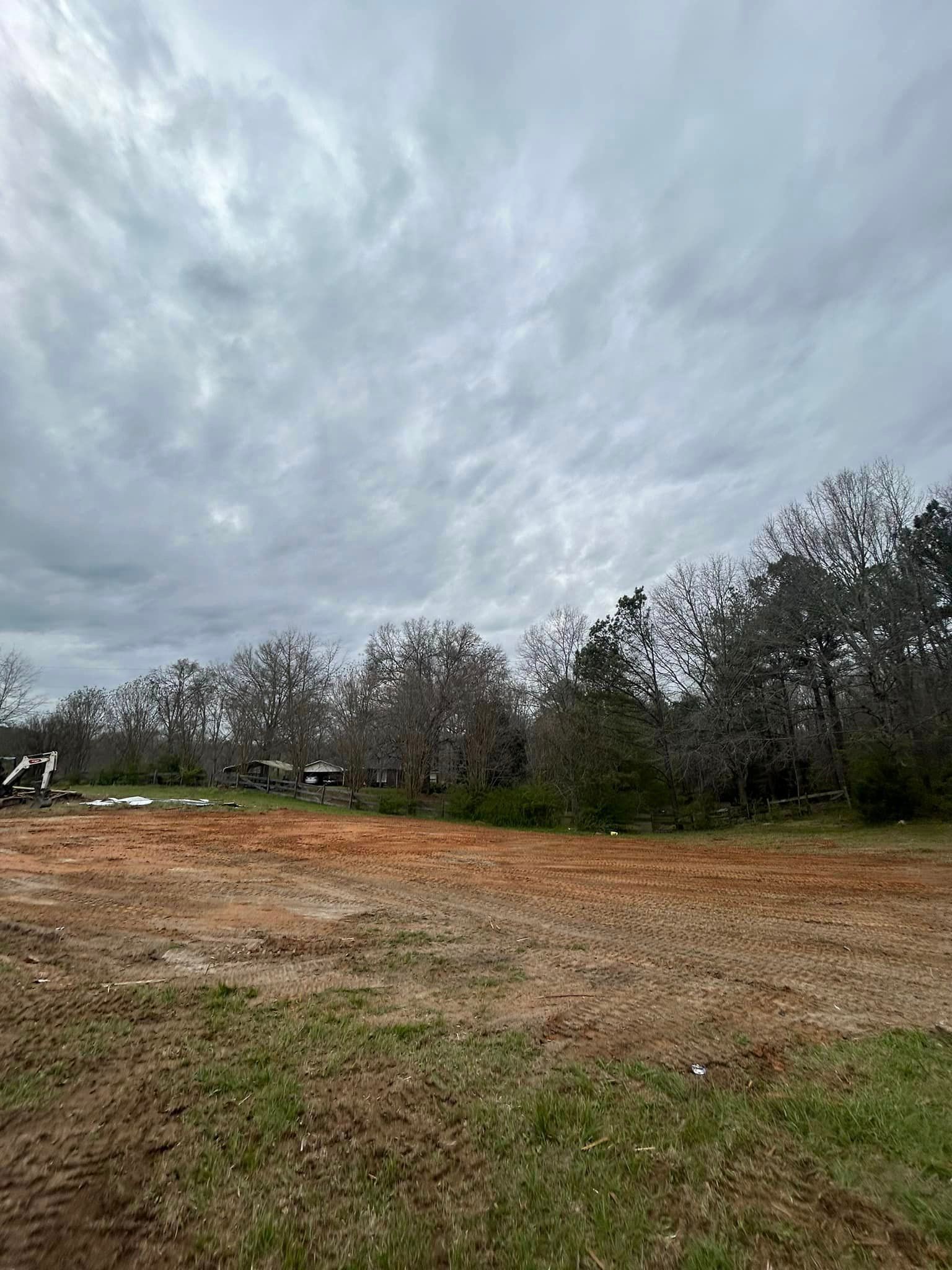 A large dirt field with trees in the background and a cloudy sky.