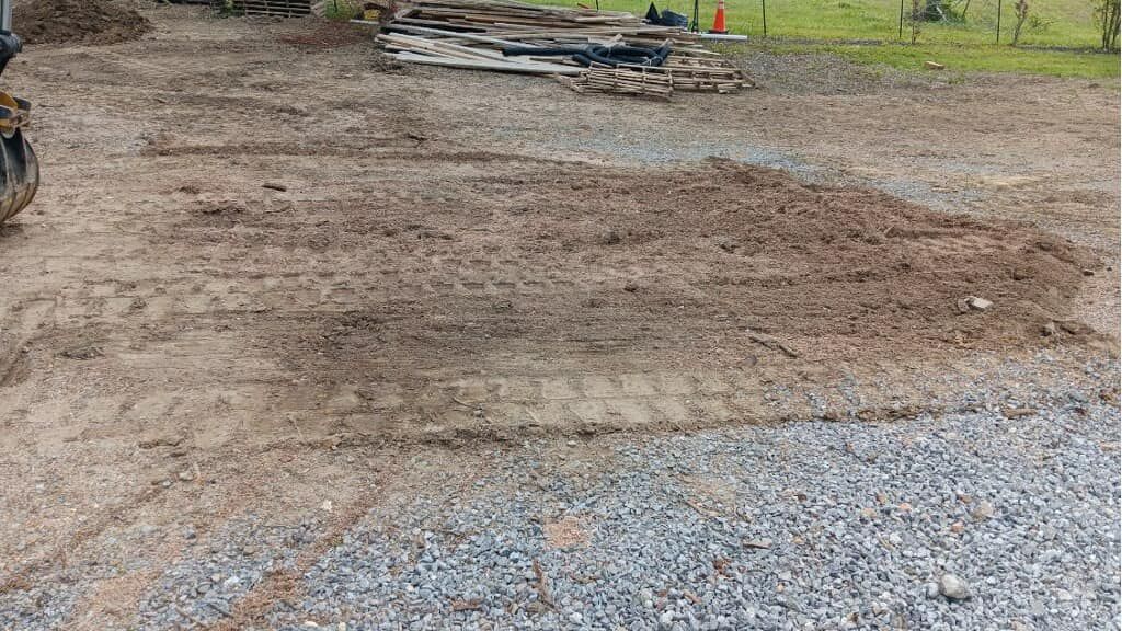 A dirt road with gravel and a tractor in the background.
