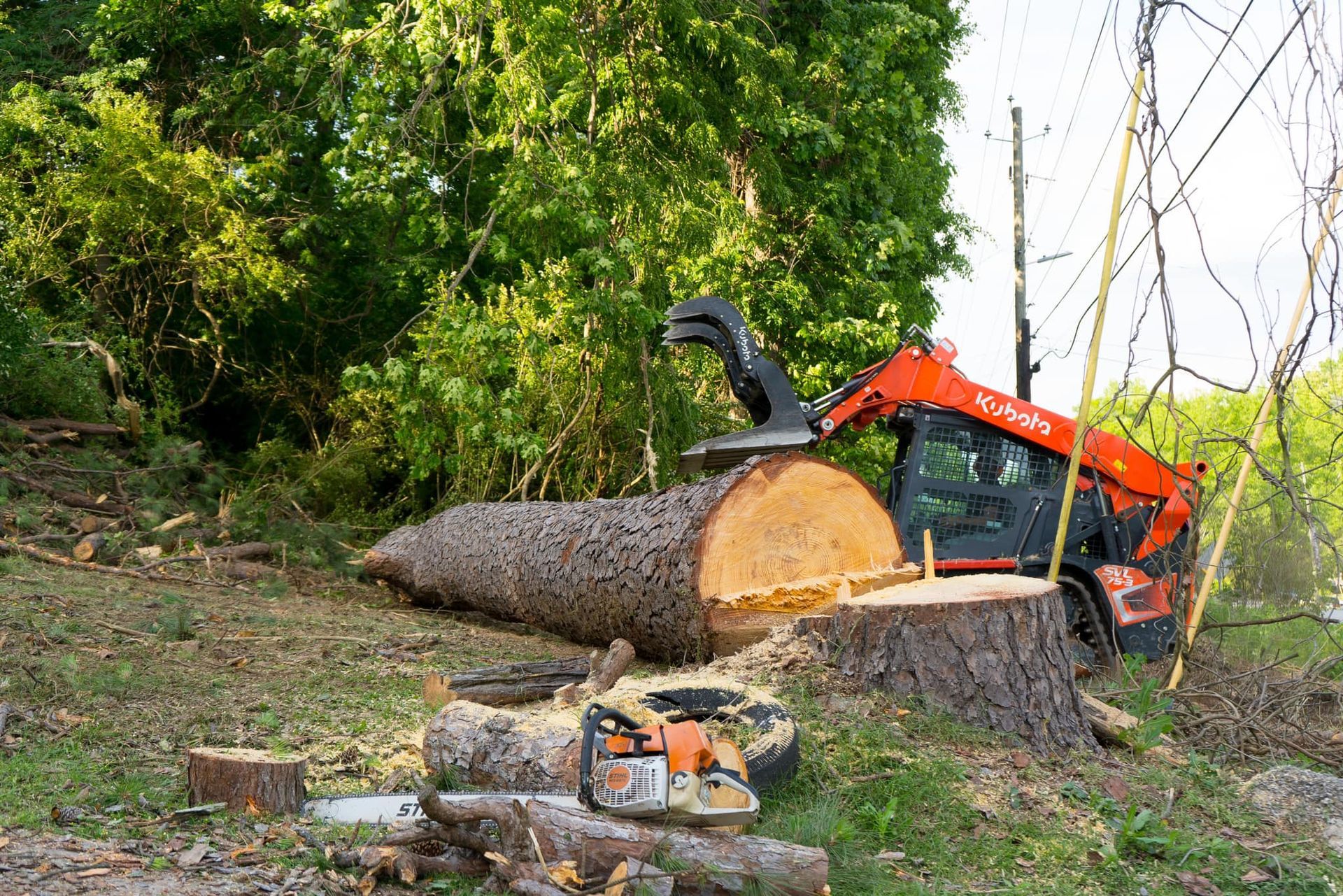 A large log is being cut down by a tractor and a chainsaw.