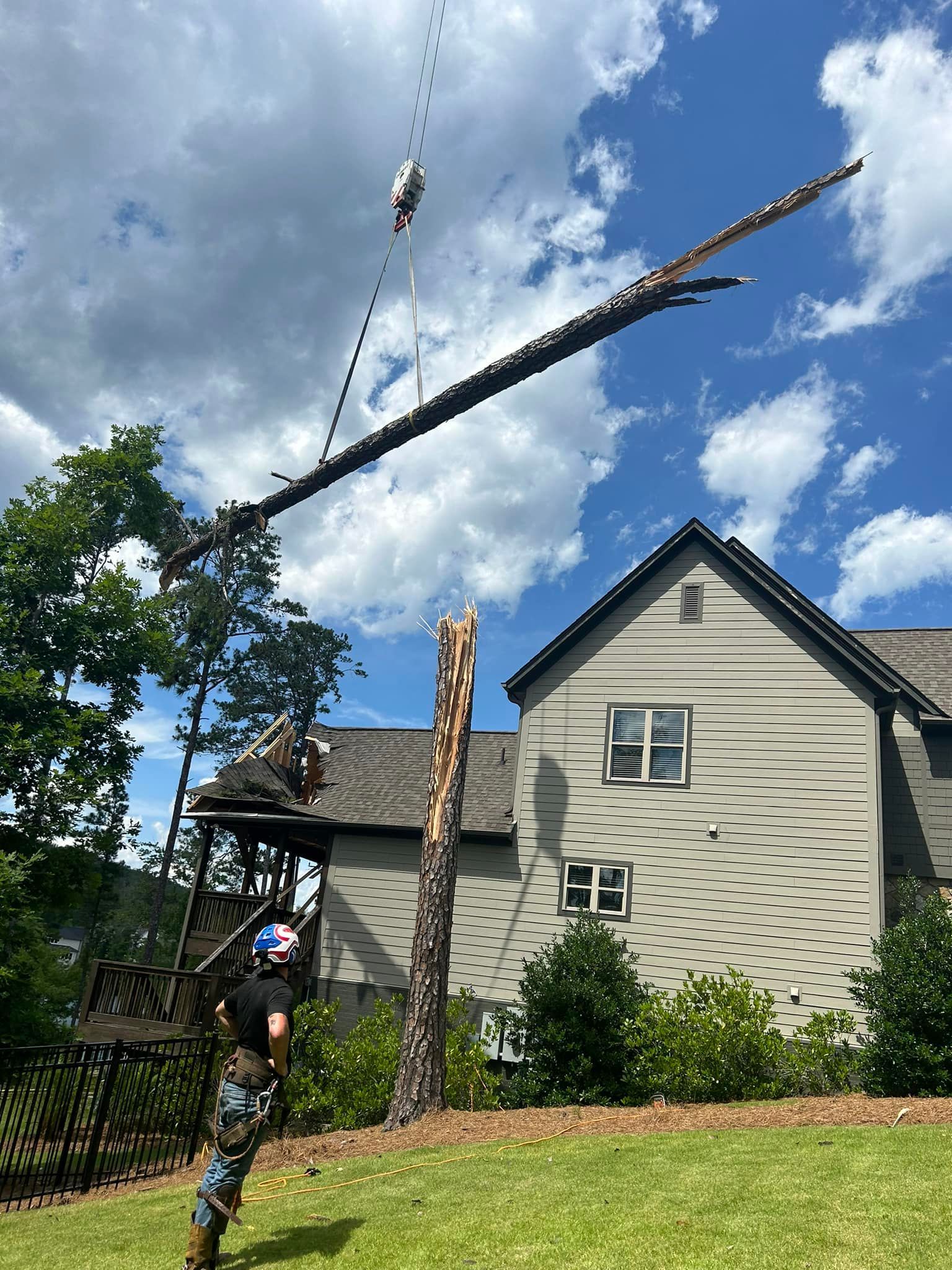 A man is standing in front of a house with a crane lifting a tree branch.