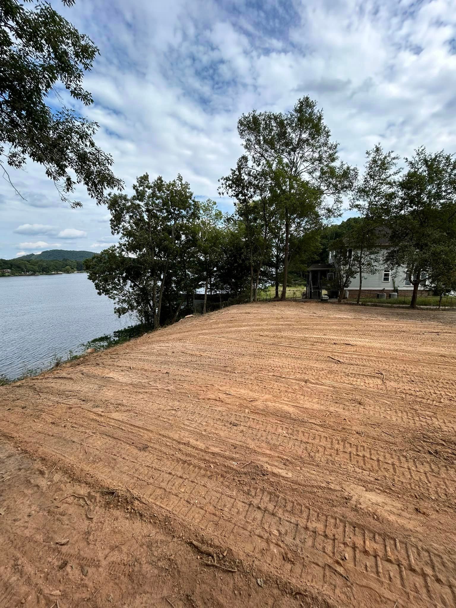 A dirt road leading to a lake with a house in the background.