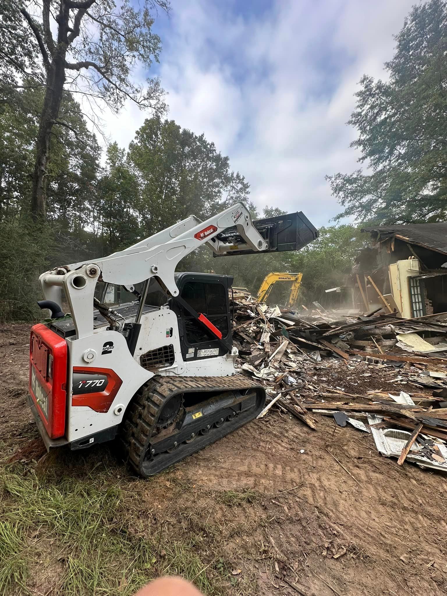 Bobcat skid-steer clears debris from a partially demolished building in an outdoor setting.