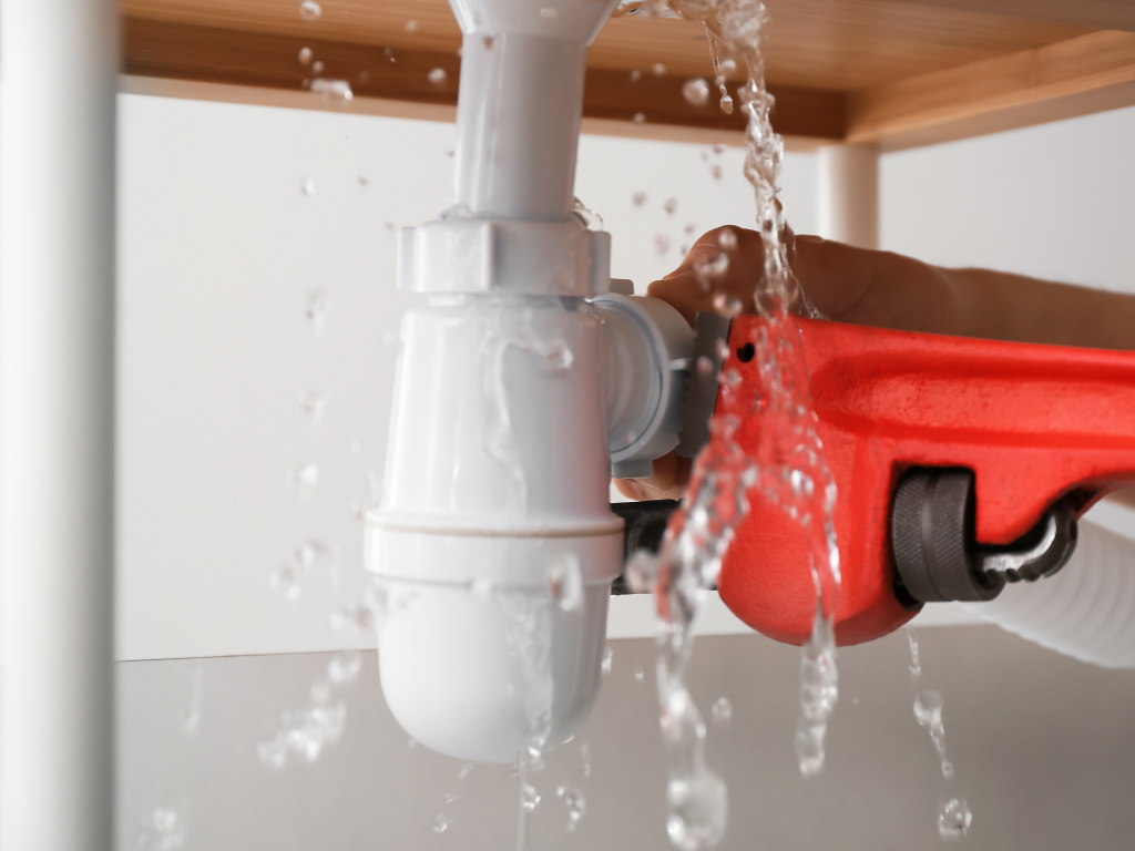 Iemand repareert een lekkende gootsteenleiding met een sleutel.