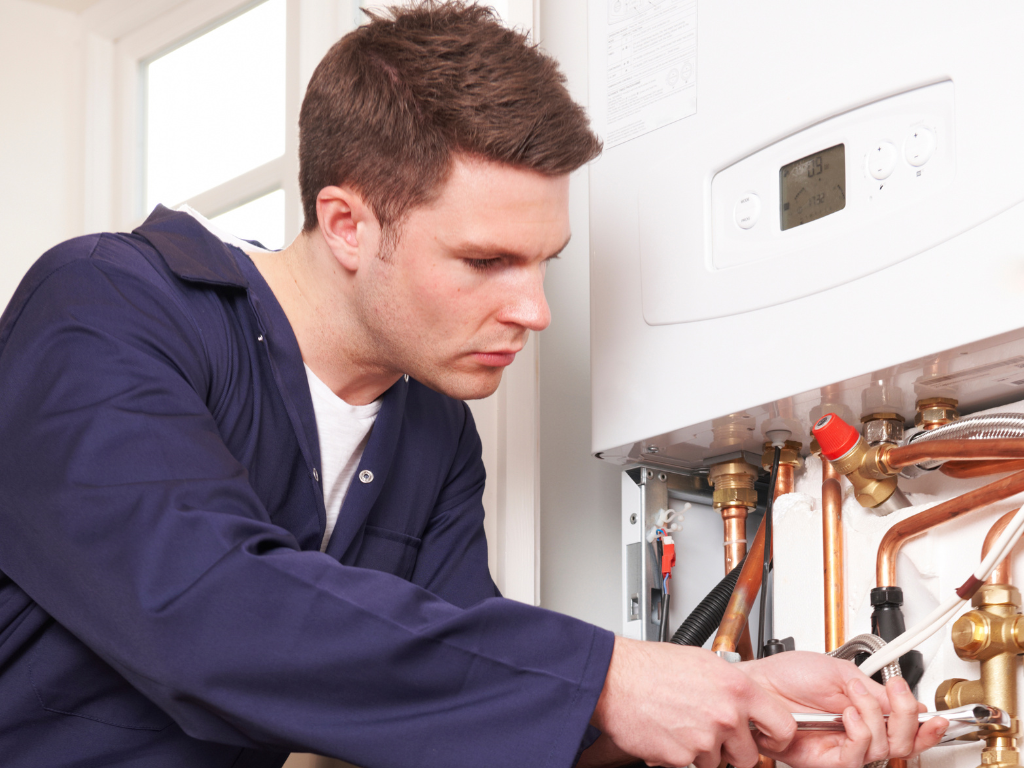 Een man werkt aan een ketel met een sleutel.