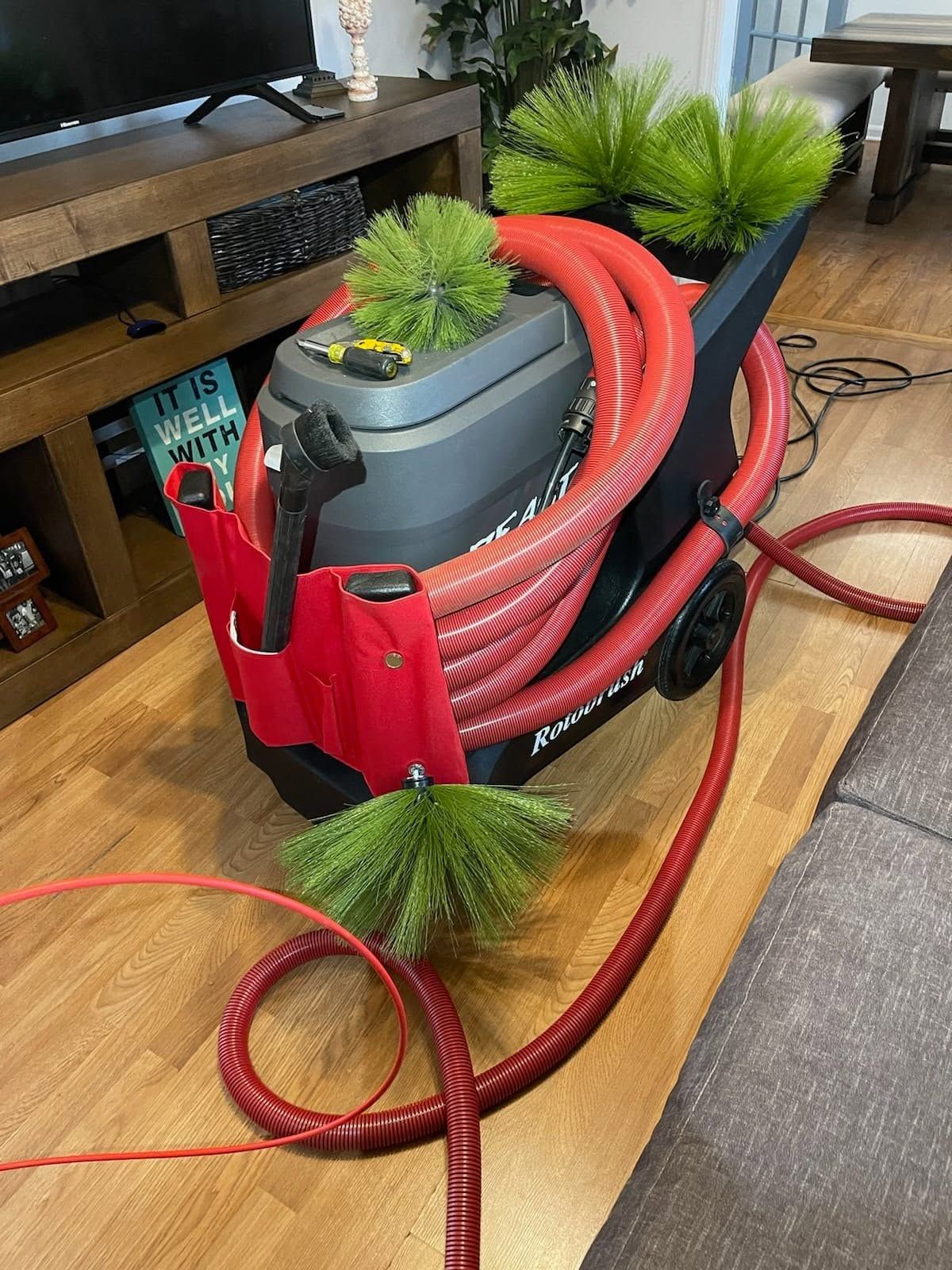 Red vacuum hose coiled in a red bag beside a plant pot on a wooden floor