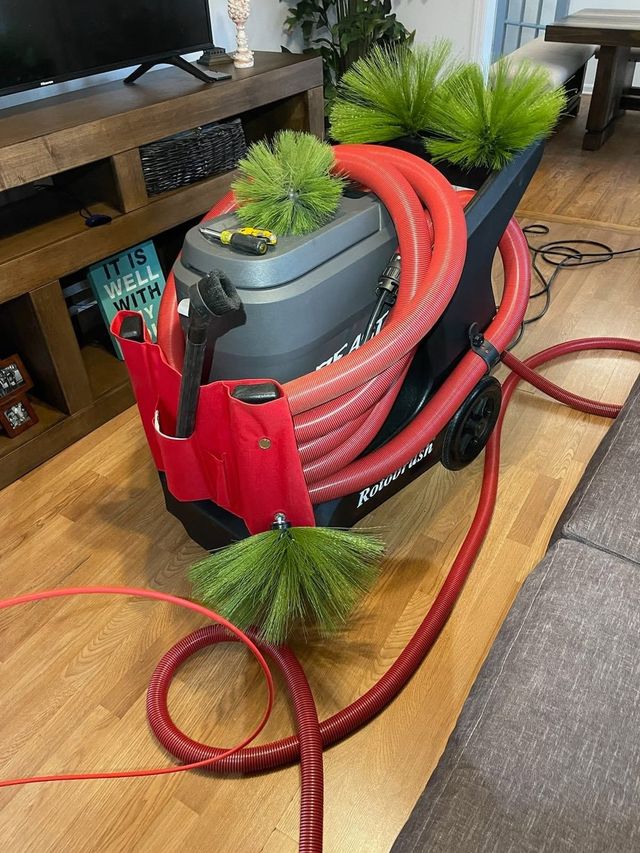 Red vacuum hose coiled in a red bag beside a plant pot on a wooden floor