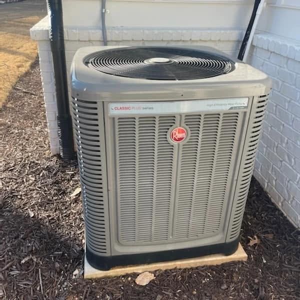 Outdoor HVAC air conditioner unit beside a white brick wall, with a fan on top.