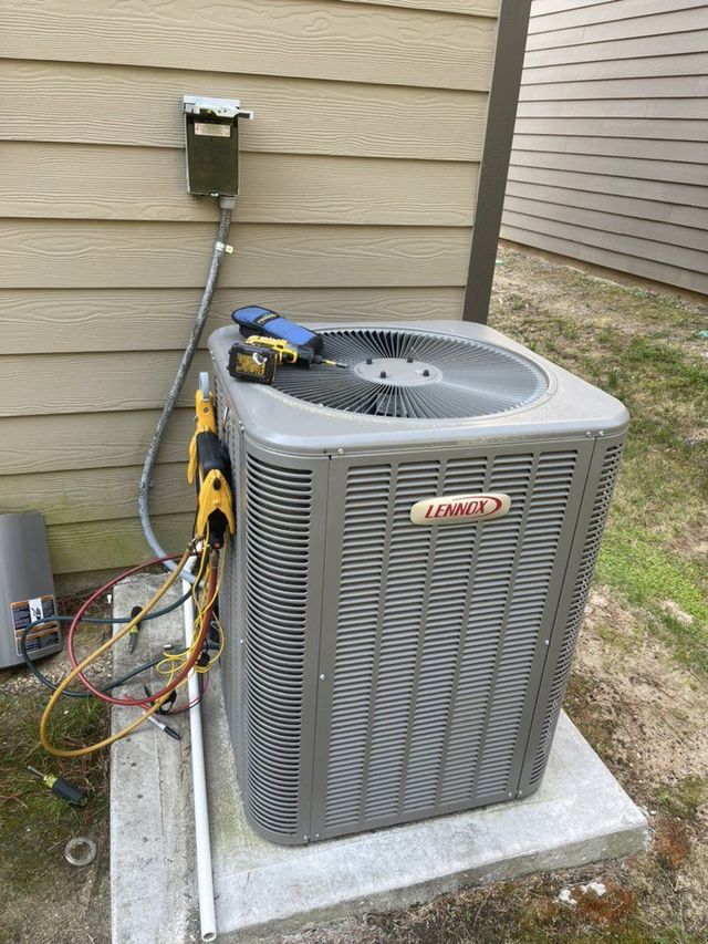 Outdoor air conditioner unit on a concrete pad beside a house, with tools and cables attached.