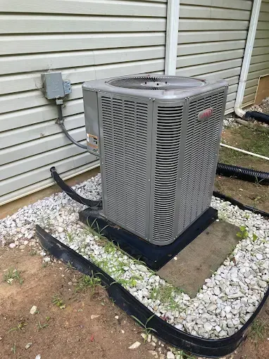 Outdoor HVAC air conditioner unit beside a white brick wall, with a fan on top.