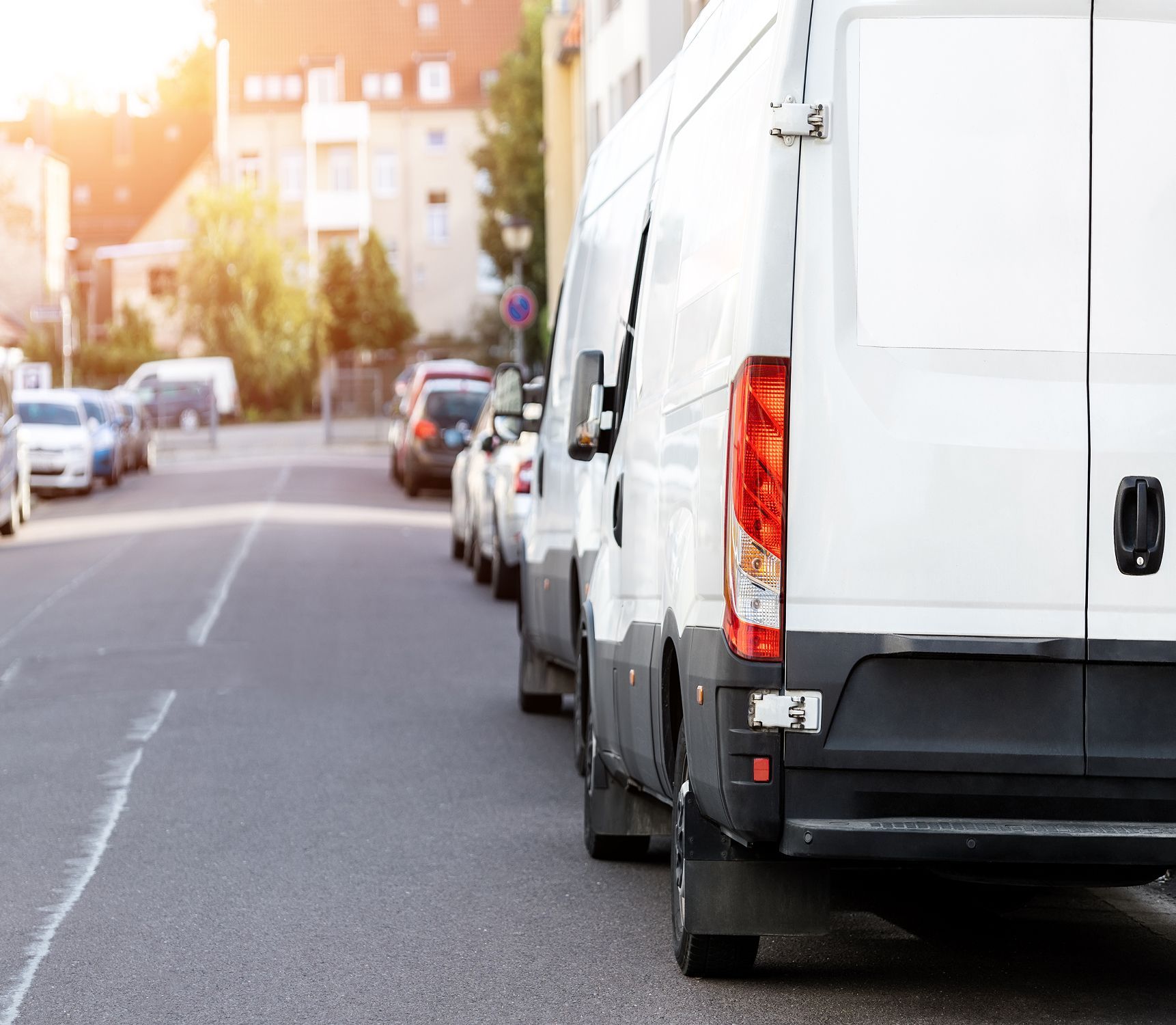 A row of white vans are parked on the side of the road.