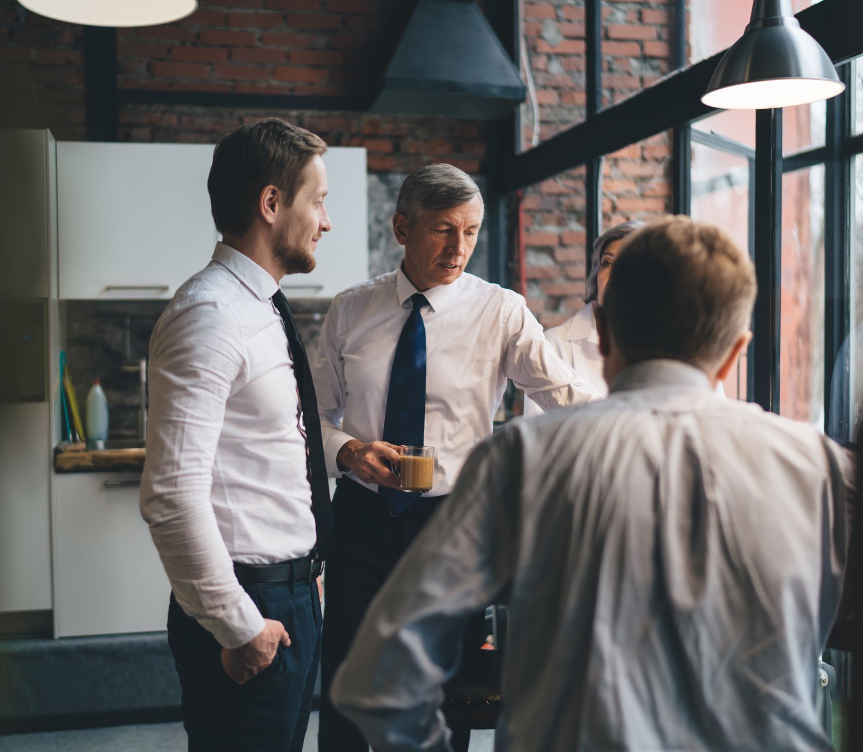 A group of men are standing in front of a window talking to each other.