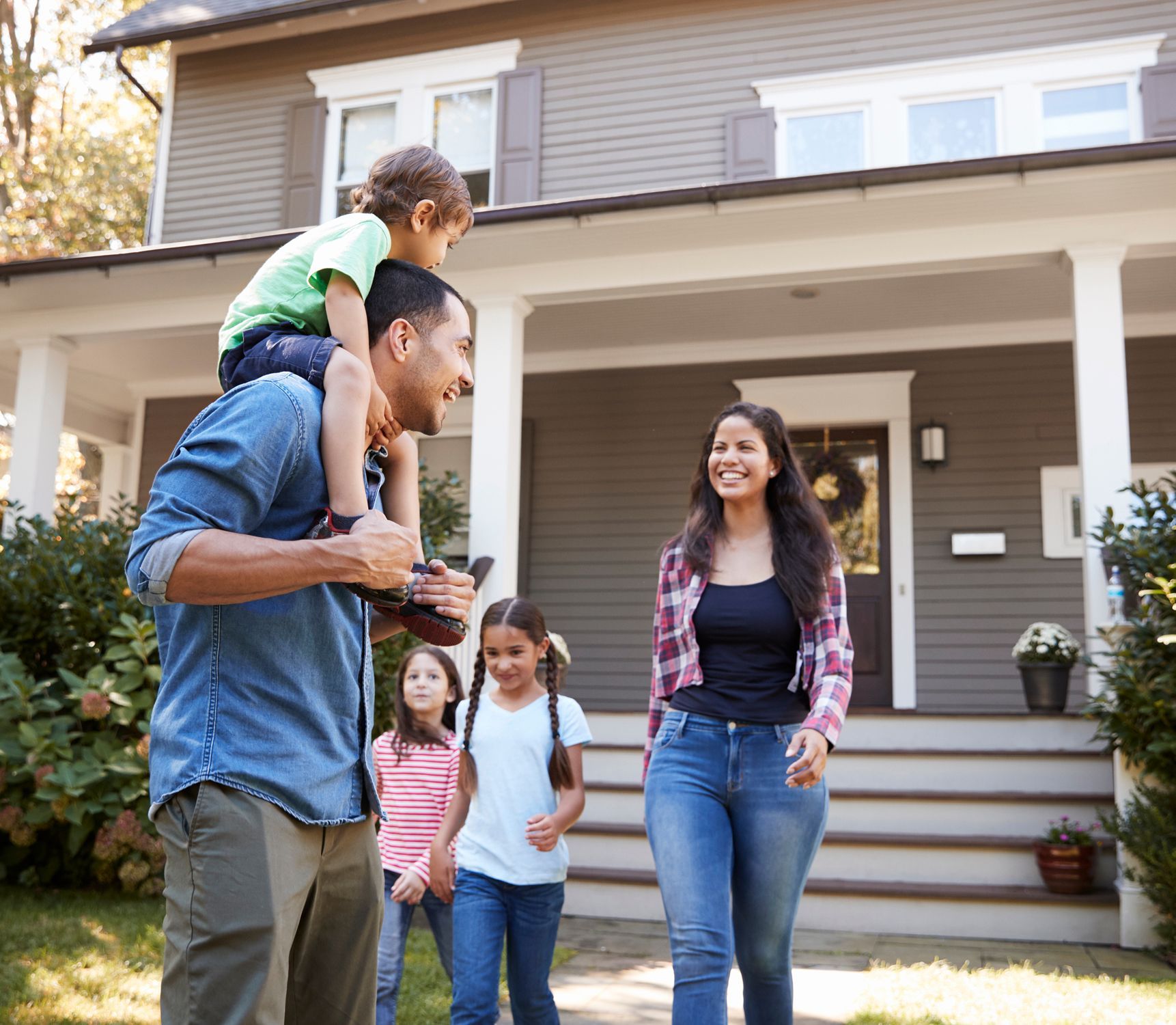 A man is carrying a child on his shoulders in front of a house.