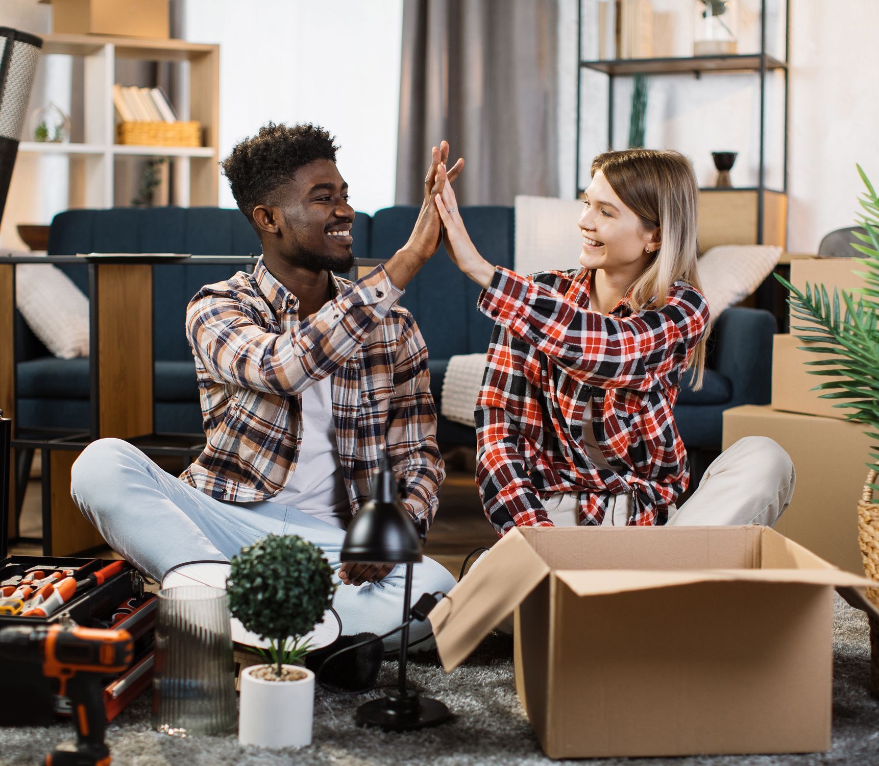A man and a woman are giving each other a high five while sitting on the floor in a living room.