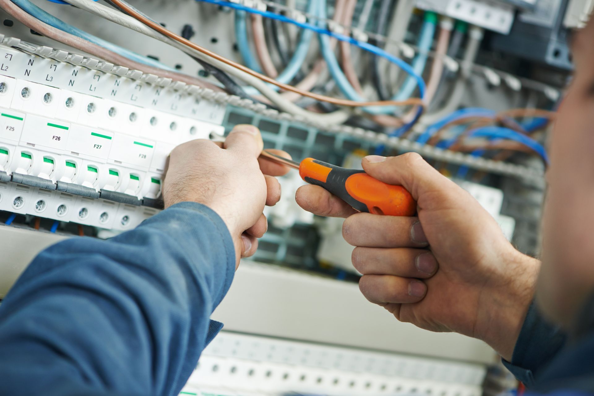 A man is working on an electrical box with a screwdriver.