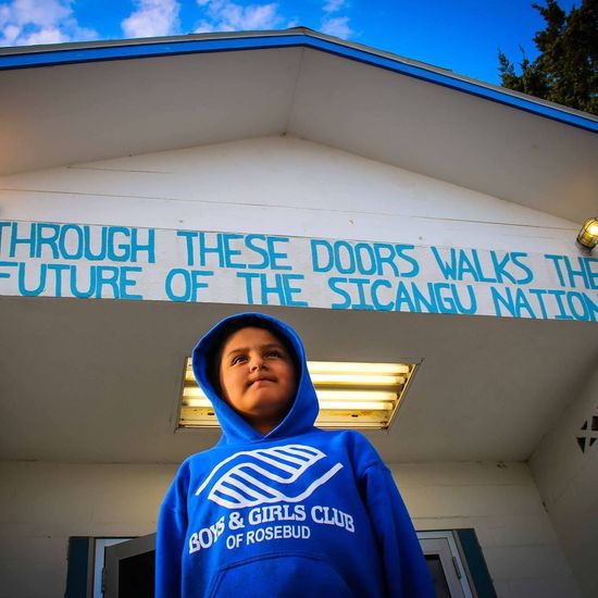 Young person in blue hoodie in front of a building with the words 