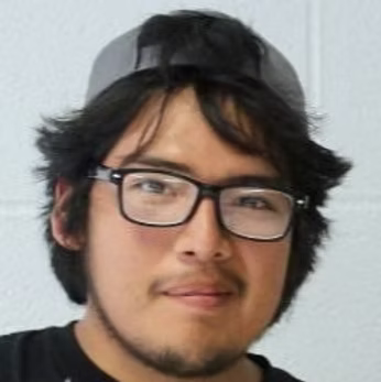 A young man with glasses, a gray cap, and dark hair smiles at the camera against a white background.