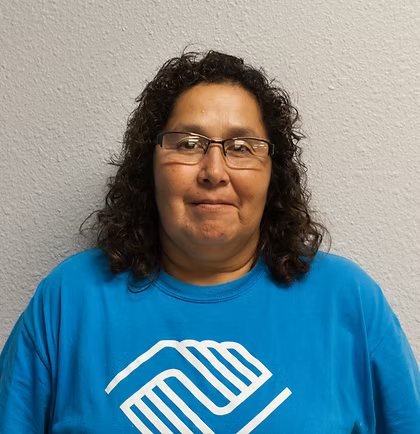 Woman wearing glasses and blue Boys & Girls Club shirt, smiling against a gray wall.