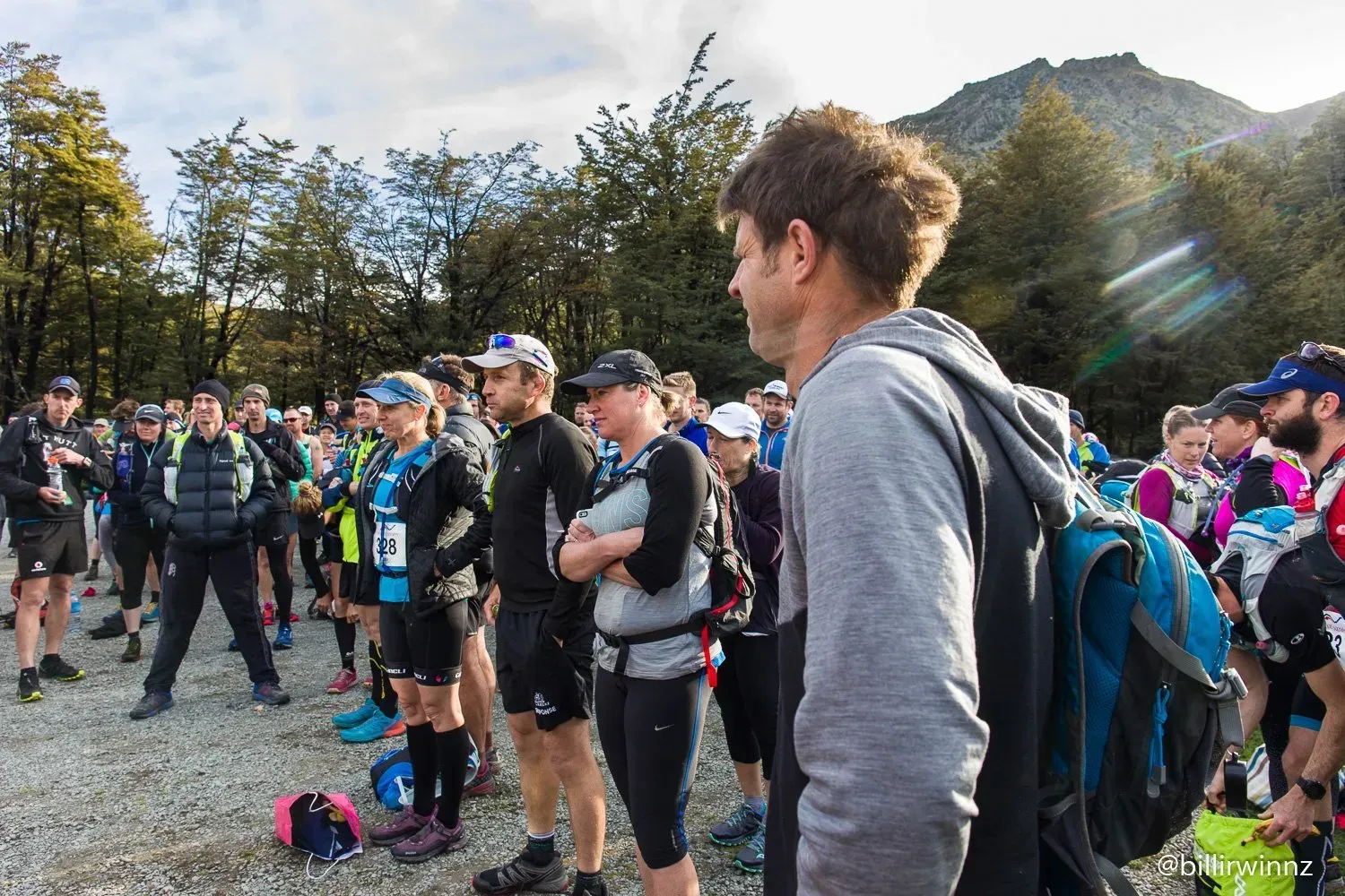 A group of people are standing in a parking lot in front of a mountain.
