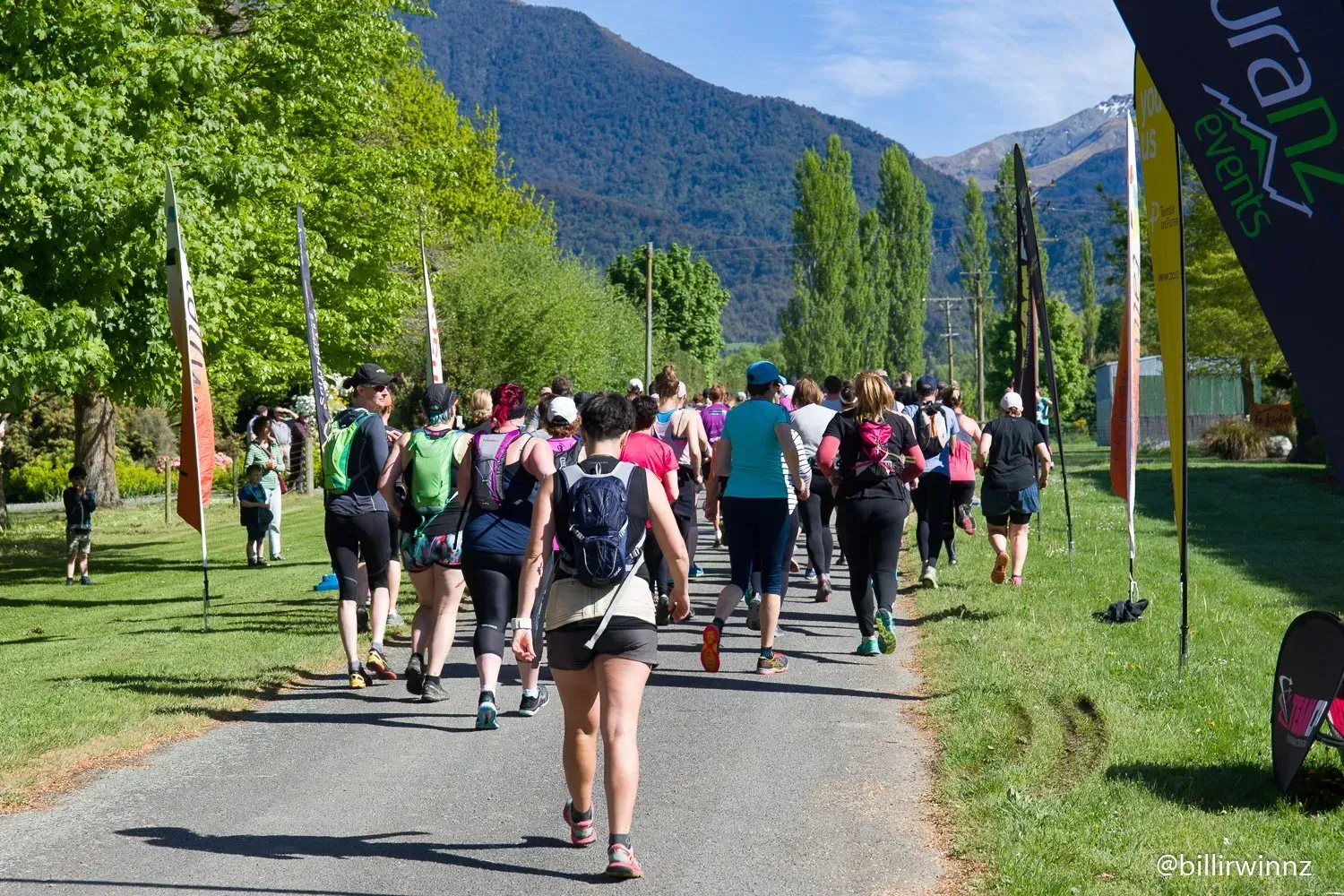 A group of people are walking down a path with mountains in the background.