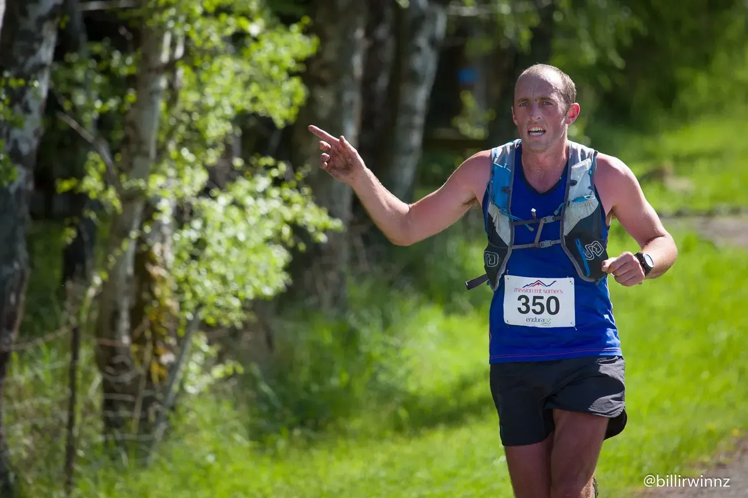 A man in a blue tank top and black shorts is running on a trail.